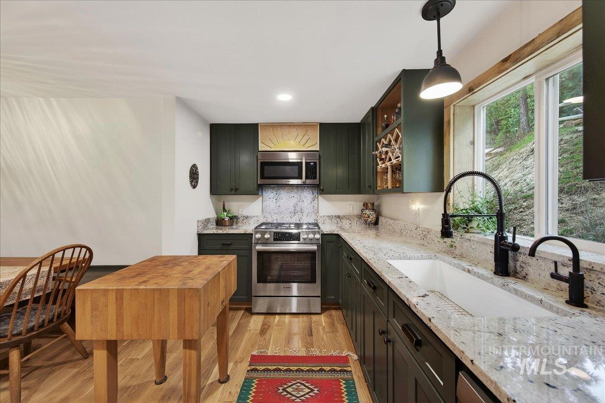 Kitchen featuring stainless steel appliances, light wood-type flooring, light stone countertops, glass insert cabinets, and pendant lighting