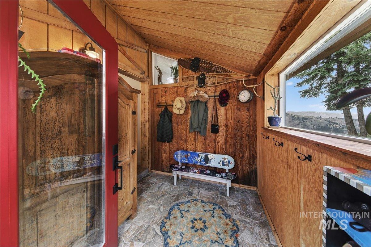 Mudroom featuring wooden walls, stone flooring, and a vaulted wooden ceiling