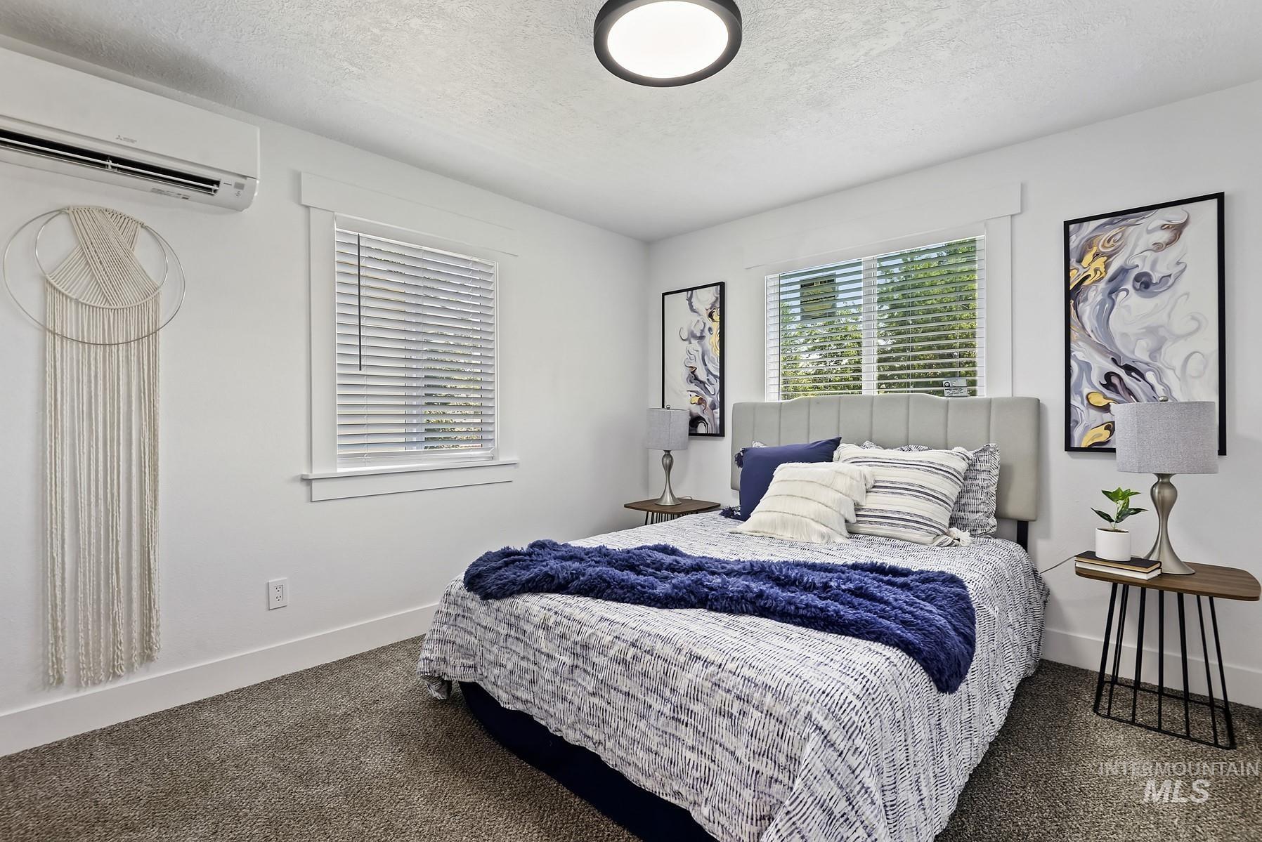 Bedroom featuring a textured ceiling, a wall mounted air conditioner, and dark carpet