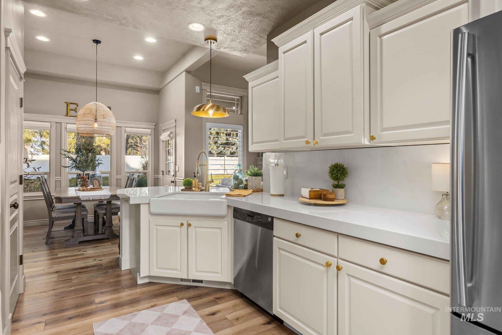 Kitchen featuring stainless steel appliances, decorative light fixtures, white cabinetry, light wood-style floors, and recessed lighting