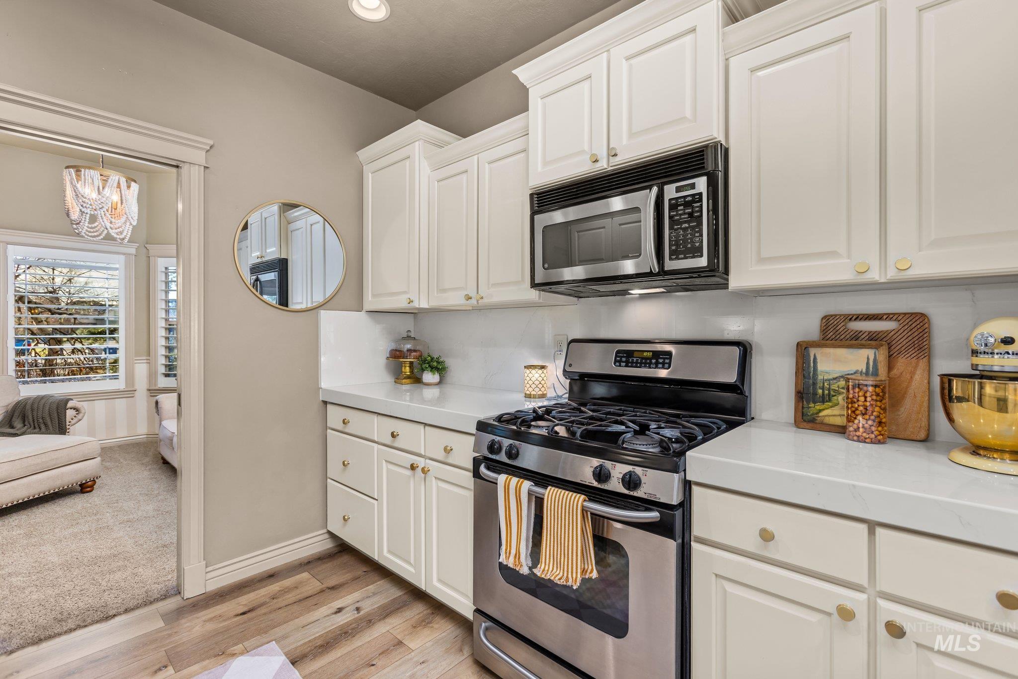 Kitchen featuring stainless steel appliances, white cabinets, light wood-style flooring, and a chandelier