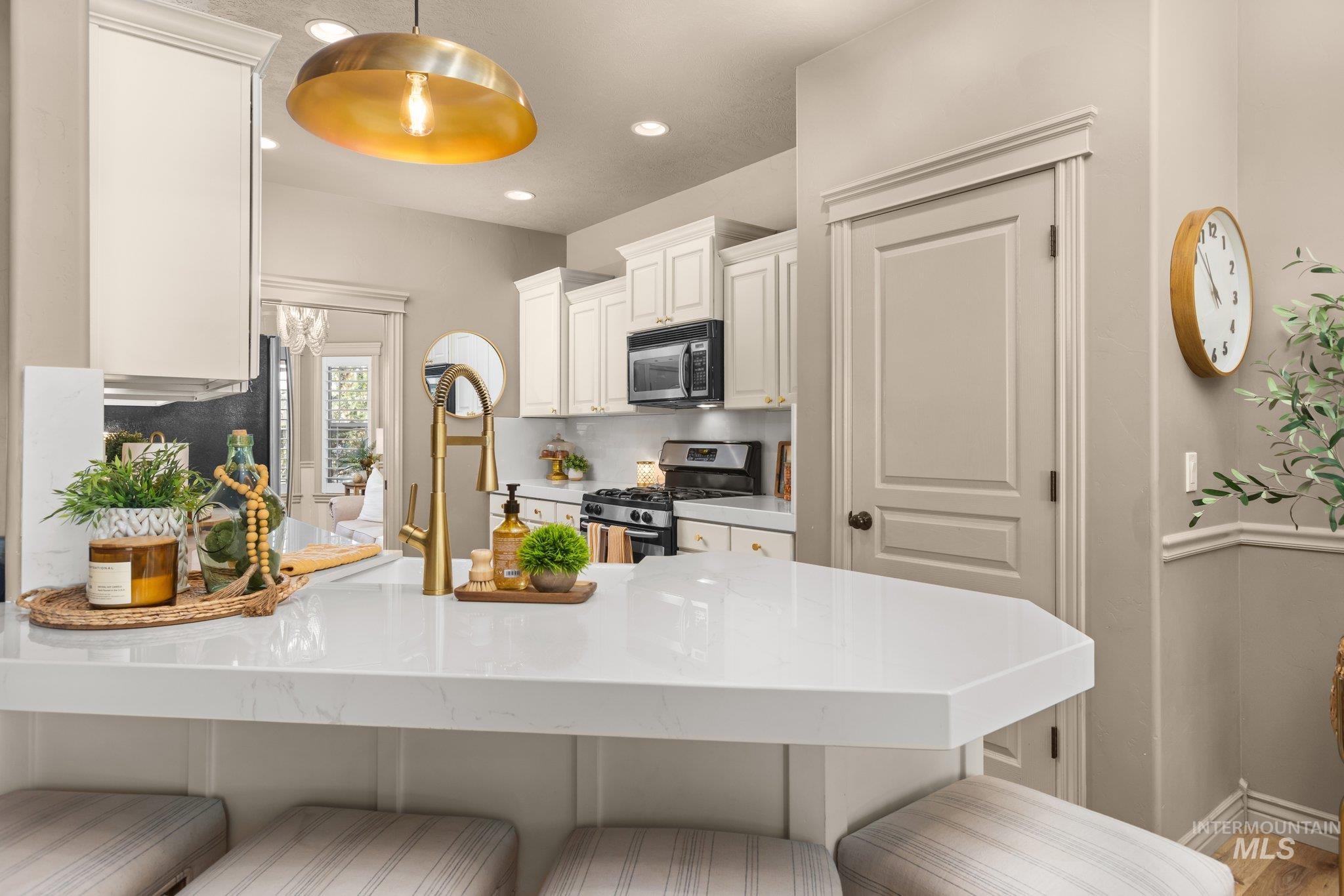 Kitchen featuring a kitchen breakfast bar, a peninsula, white cabinets, stainless steel range with gas cooktop, and black microwave