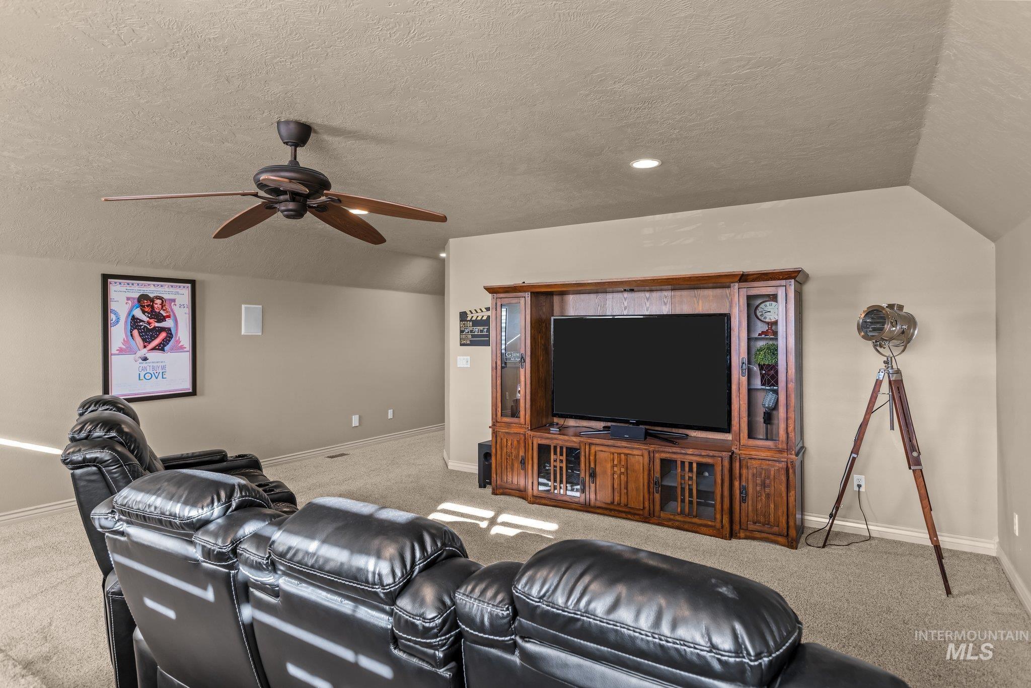 Cinema room with light carpet, a textured ceiling, vaulted ceiling, and ceiling fan