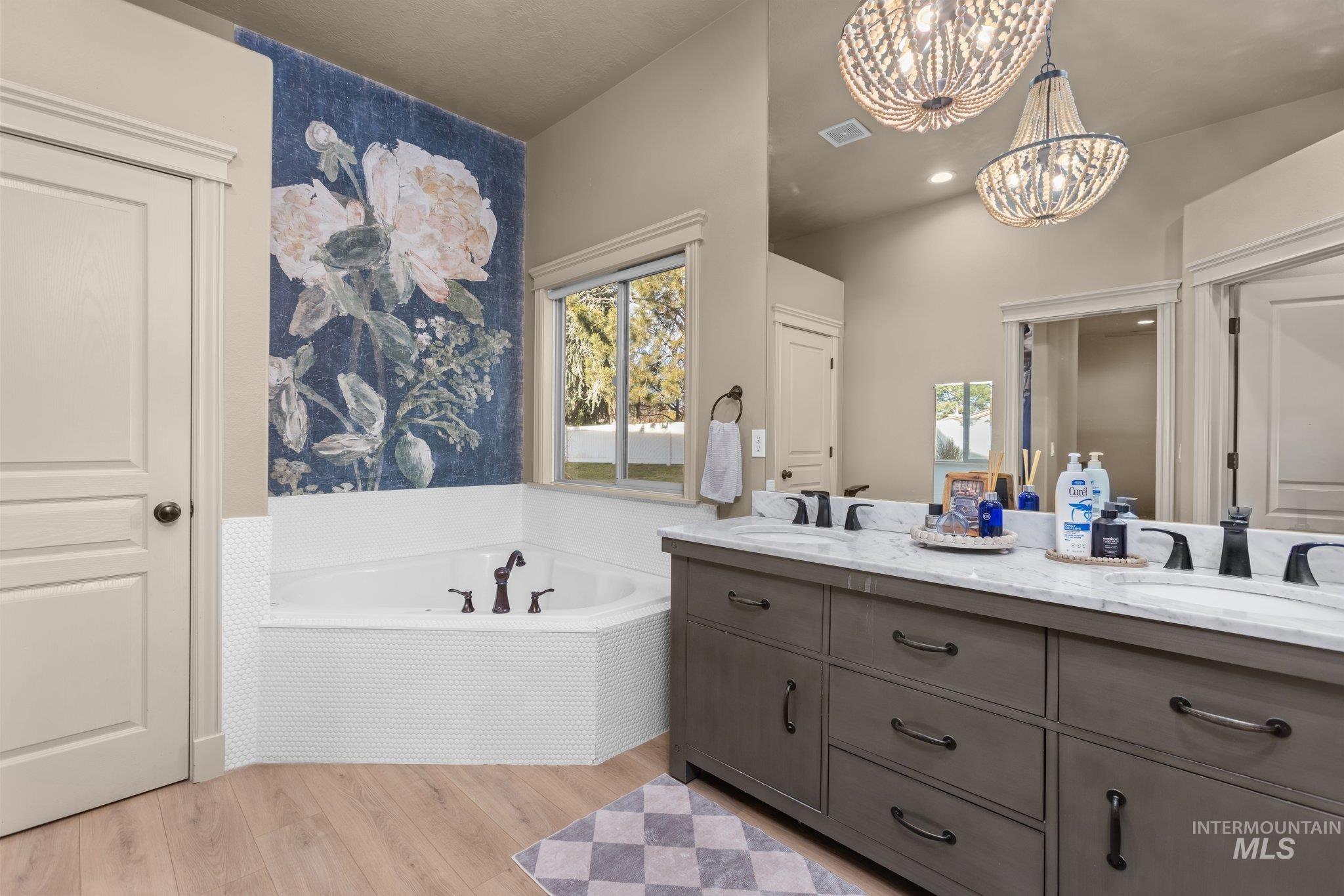 Full bath featuring double vanity, a bath, light wood finished floors, and a chandelier