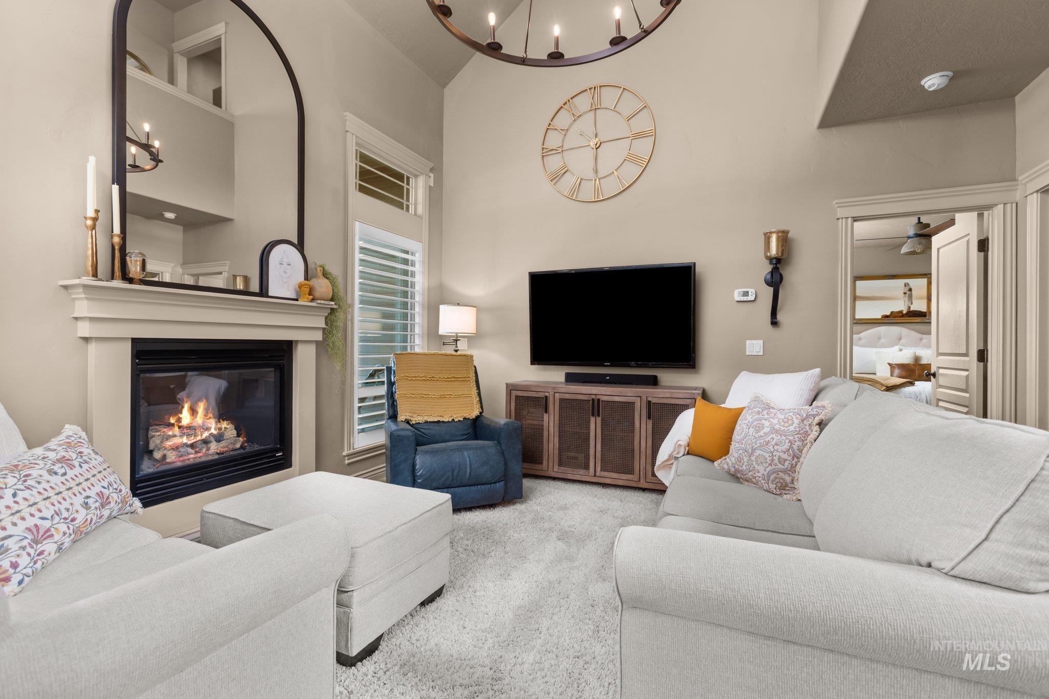 Living area with a glass covered fireplace, a towering ceiling, a chandelier, and carpet flooring
