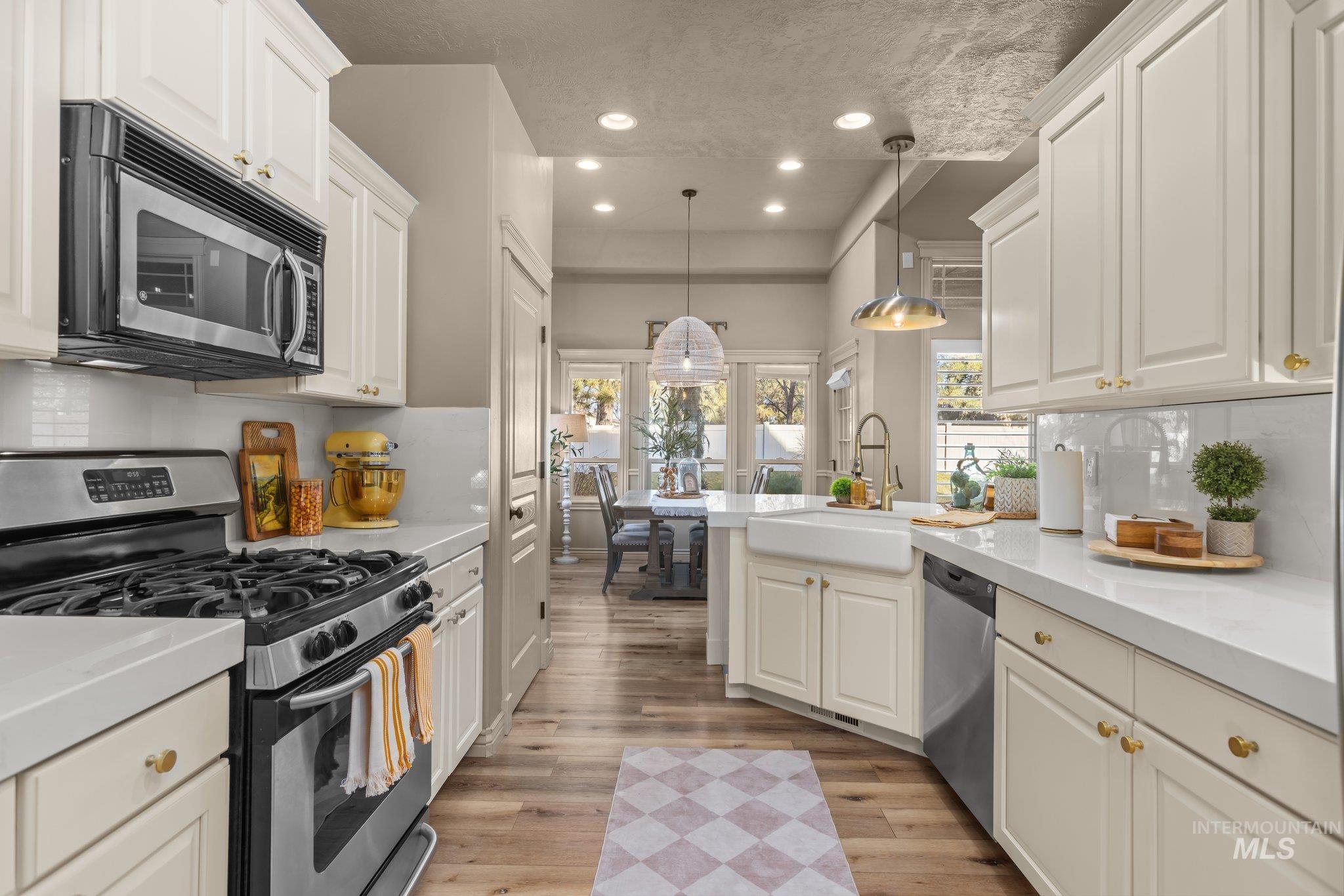 Kitchen featuring backsplash, appliances with stainless steel finishes, hanging light fixtures, a peninsula, and recessed lighting