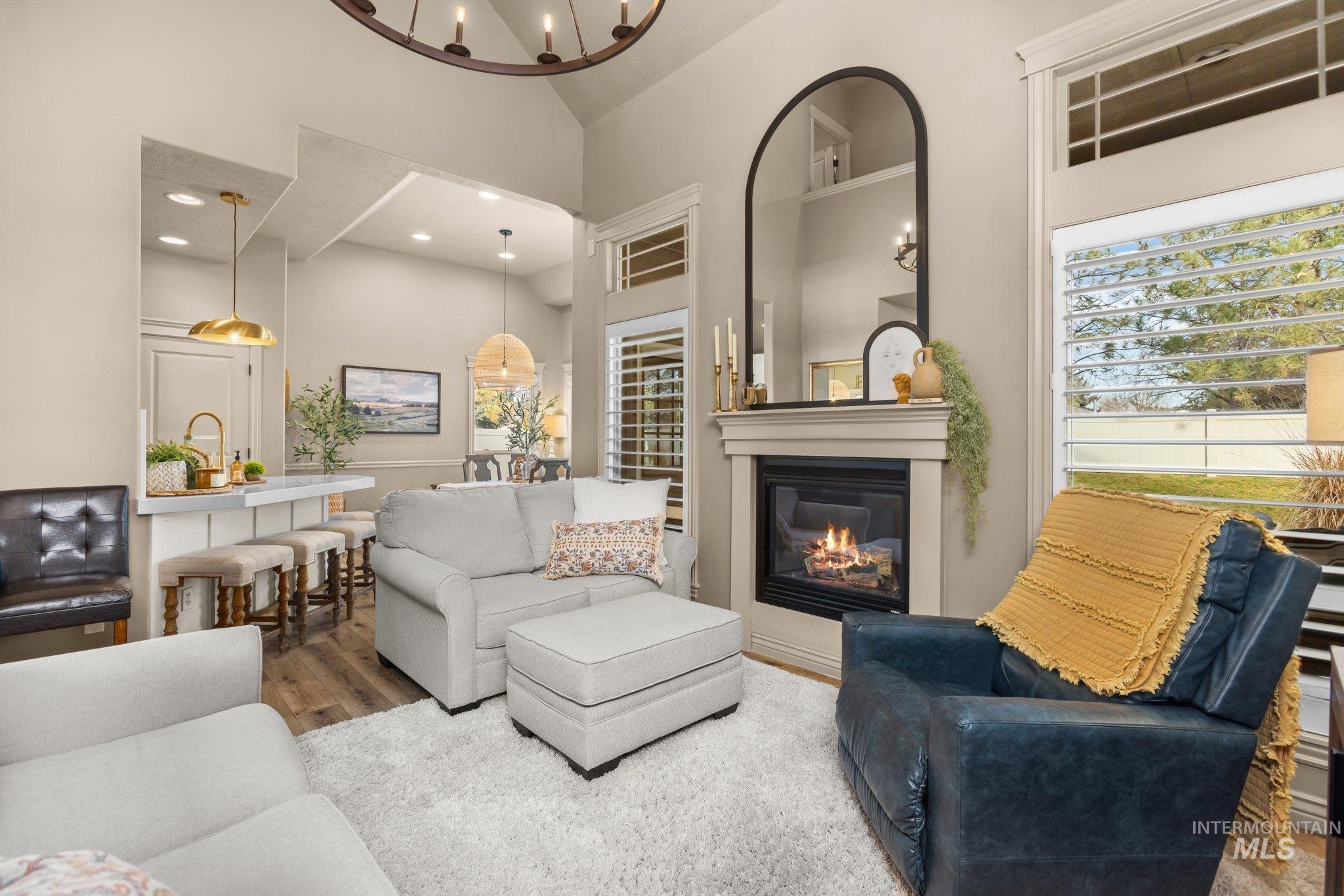 Living room with wood finished floors, a glass covered fireplace, high vaulted ceiling, a chandelier, and recessed lighting