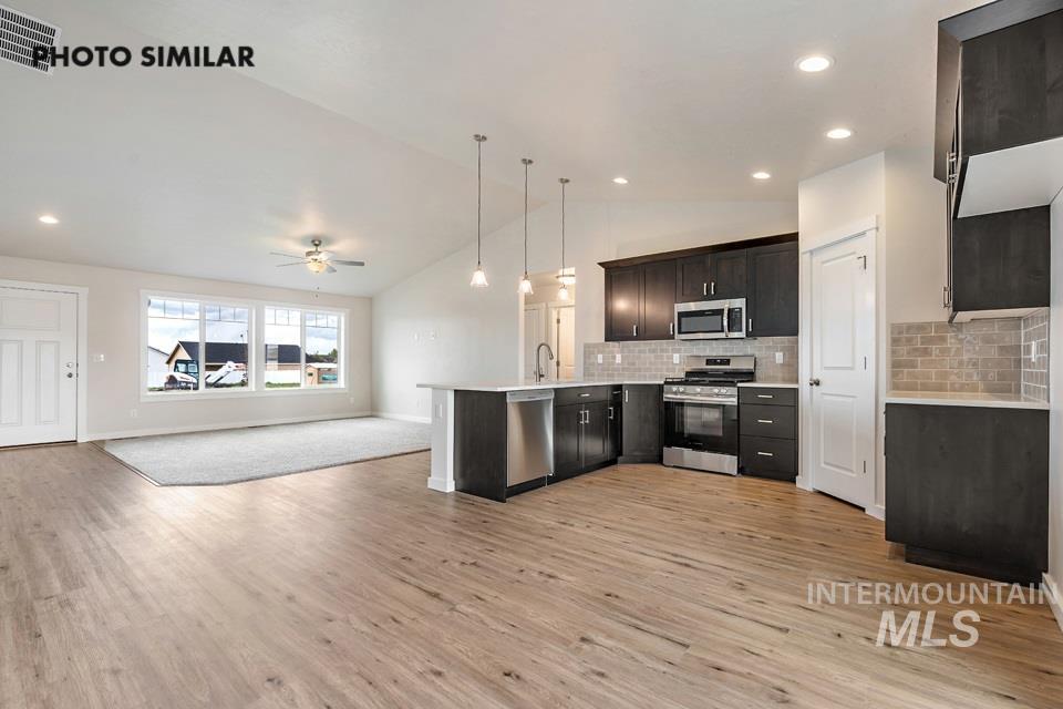 Kitchen with open floor plan, stainless steel appliances, lofted ceiling, decorative backsplash, and pendant lighting
