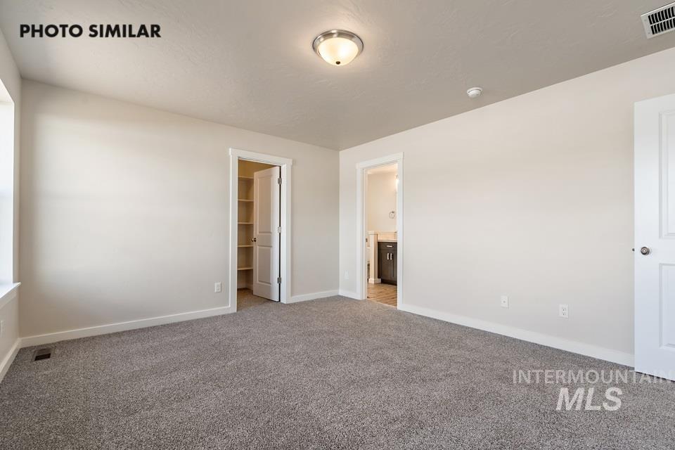 Unfurnished bedroom with a walk in closet, carpet floors, and ensuite bathroom