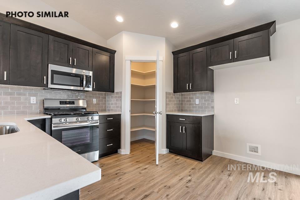 Kitchen featuring appliances with stainless steel finishes, backsplash, light wood-style floors, light stone counters, and recessed lighting