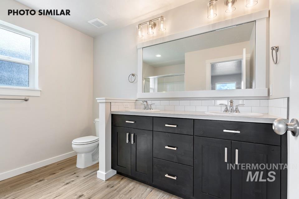 Bathroom featuring tasteful backsplash, double vanity, a shower stall, and light wood-style flooring