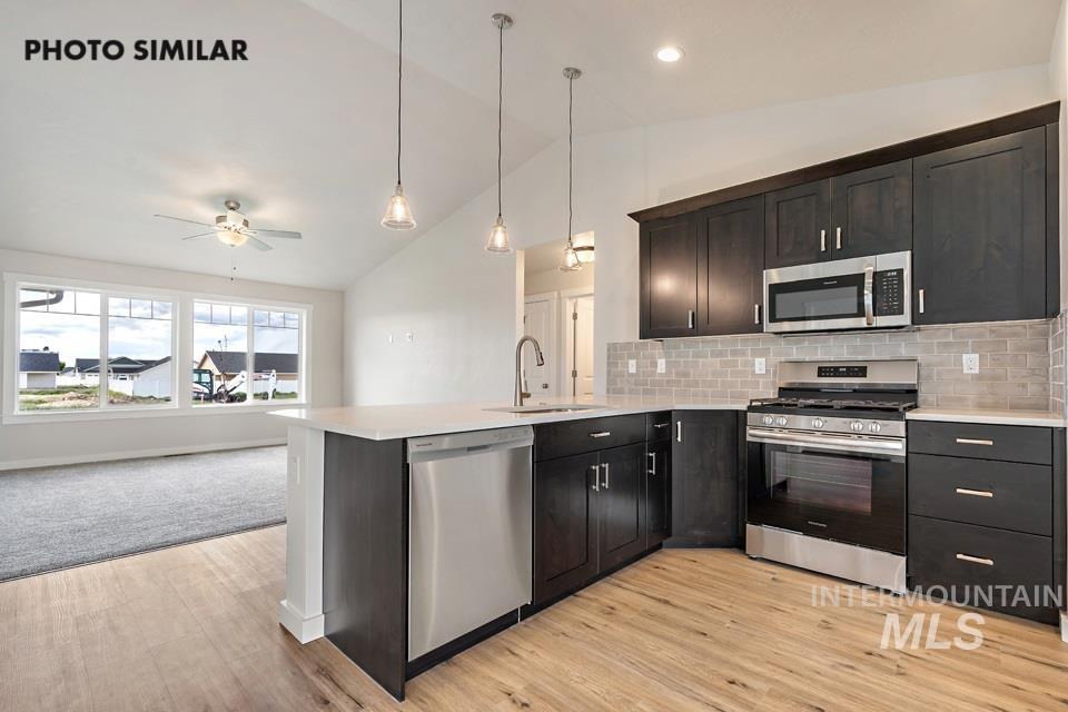 Kitchen featuring lofted ceiling, appliances with stainless steel finishes, tasteful backsplash, open floor plan, and decorative light fixtures