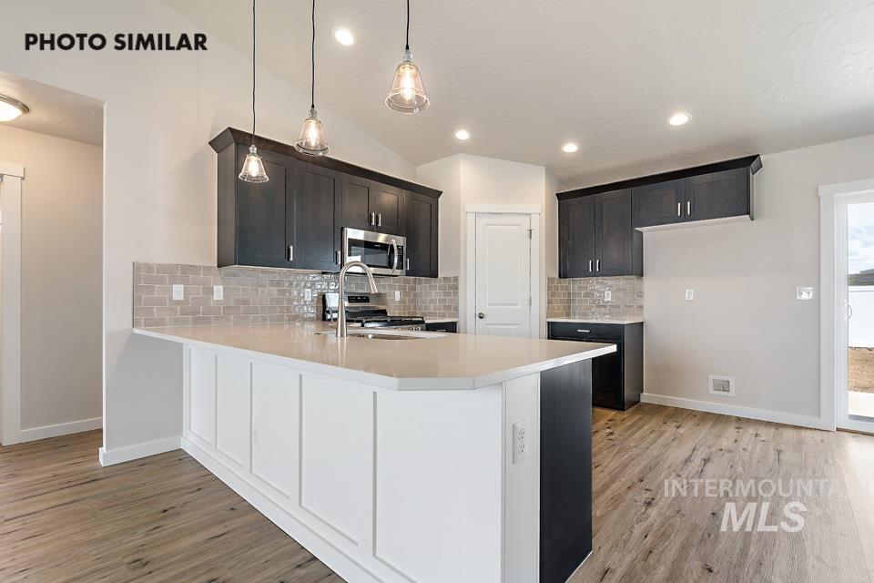 Kitchen featuring a peninsula, light wood-style flooring, hanging light fixtures, backsplash, and stainless steel appliances