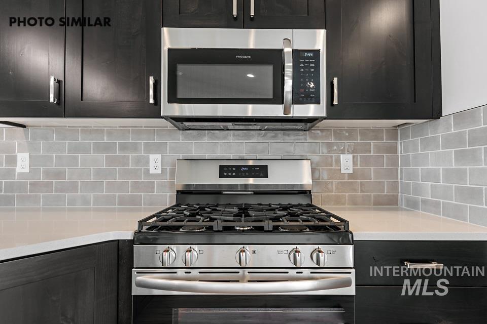 Kitchen featuring appliances with stainless steel finishes, dark cabinetry, light stone countertops, and backsplash