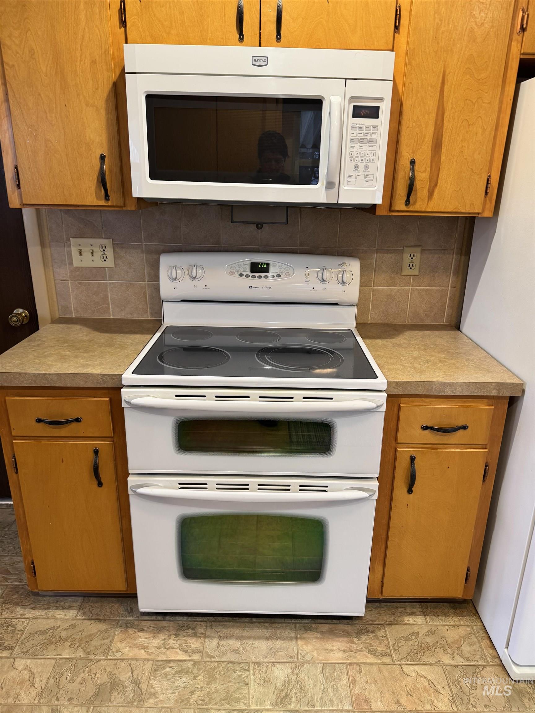 Kitchen with white appliances, brown cabinets, light countertops, and stone tile flooring