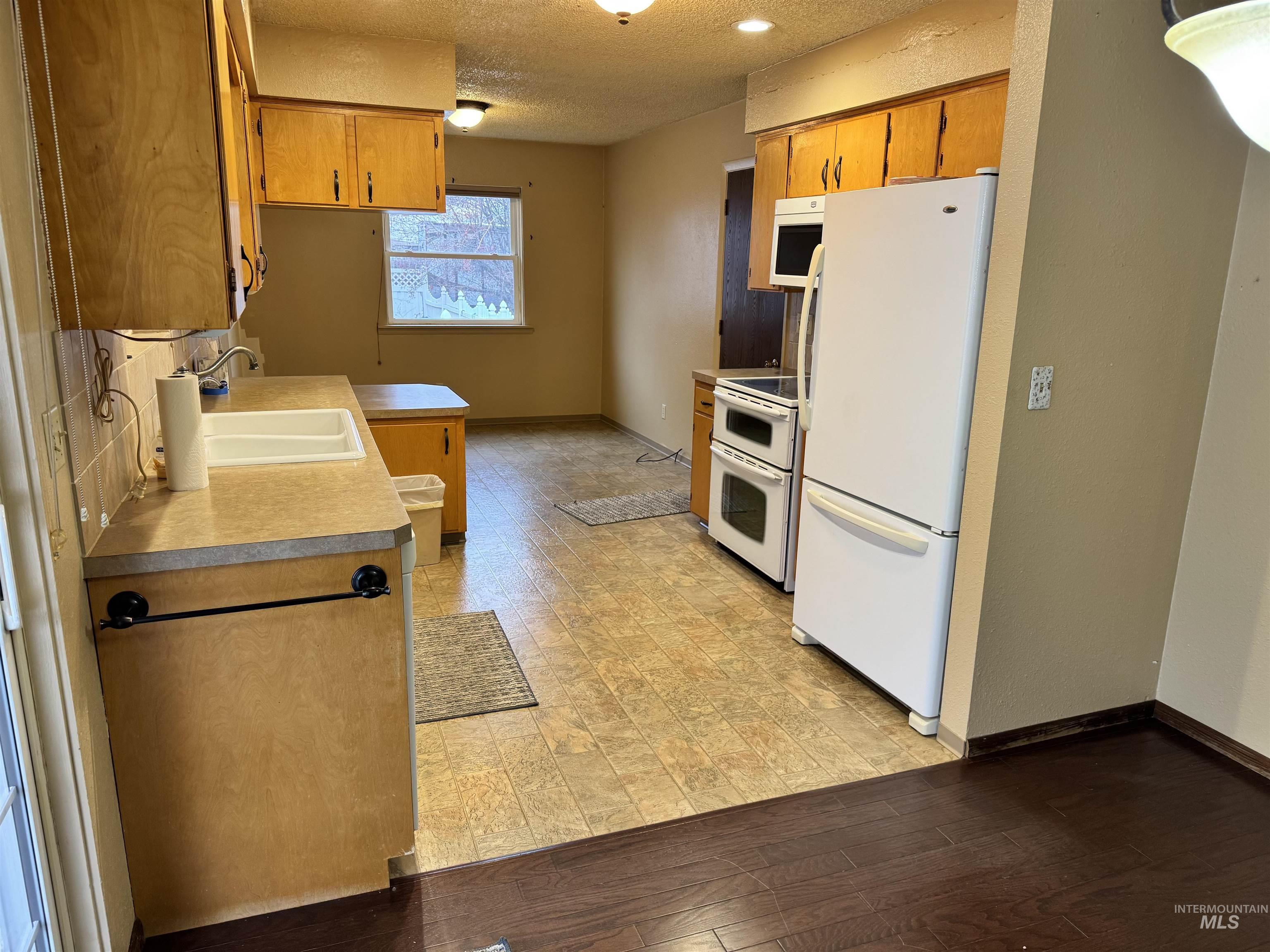 Kitchen featuring a textured ceiling, white appliances, brown cabinetry, light countertops, and light wood-style flooring