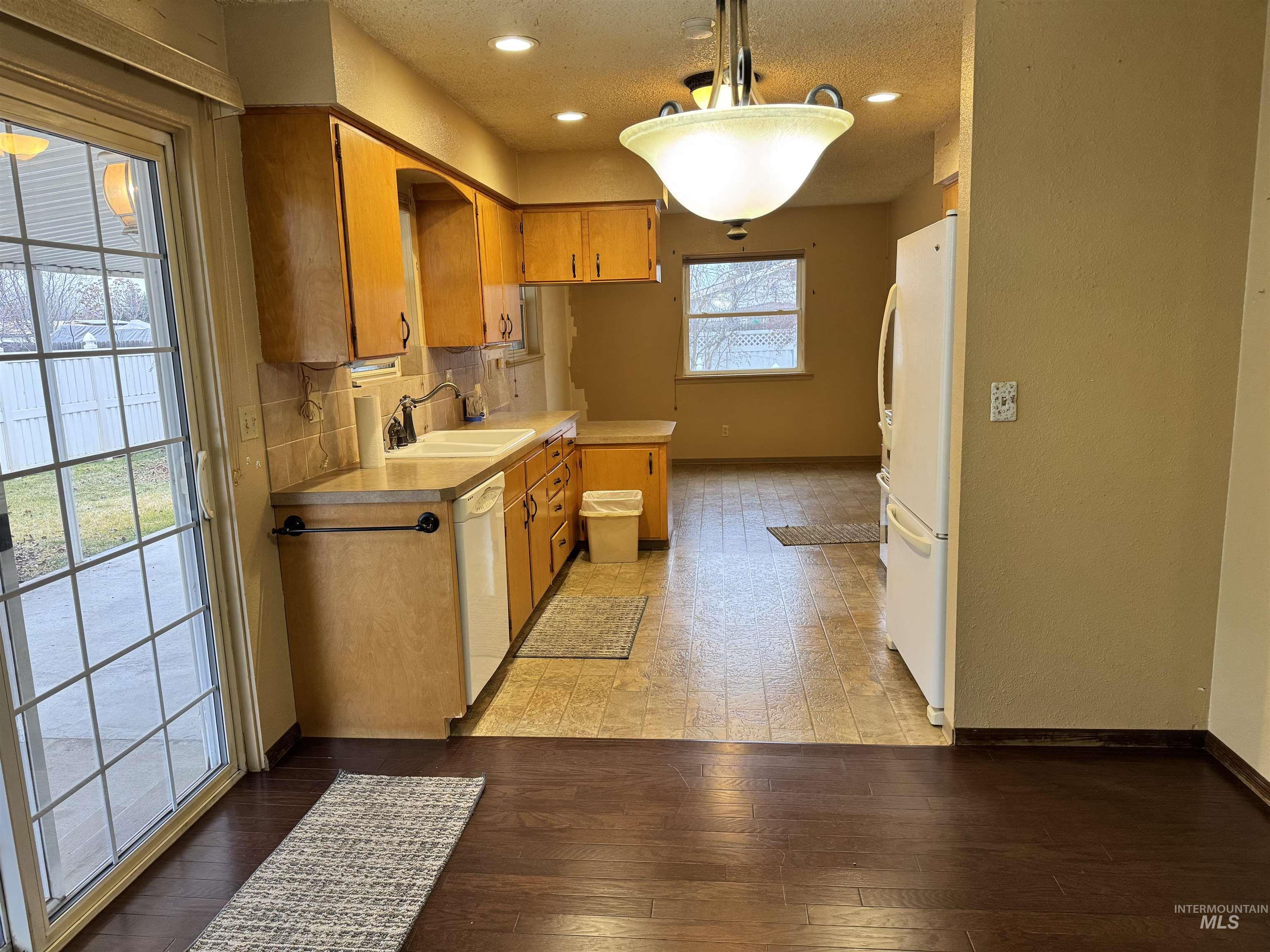 Kitchen with light countertops, decorative light fixtures, white appliances, brown cabinets, and light wood-style floors