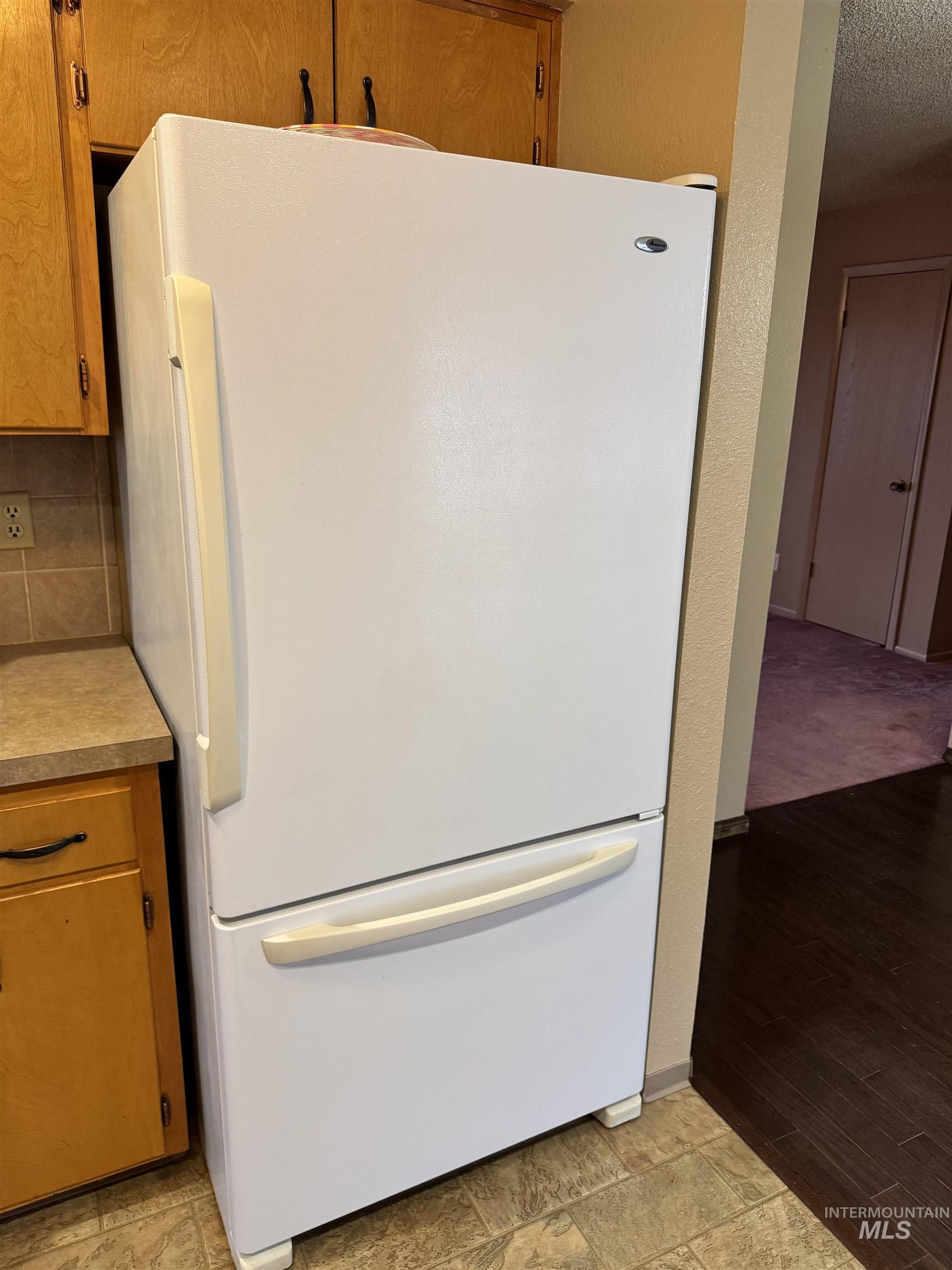 Kitchen featuring freestanding refrigerator, light countertops, brown cabinetry, a textured wall, and a textured ceiling