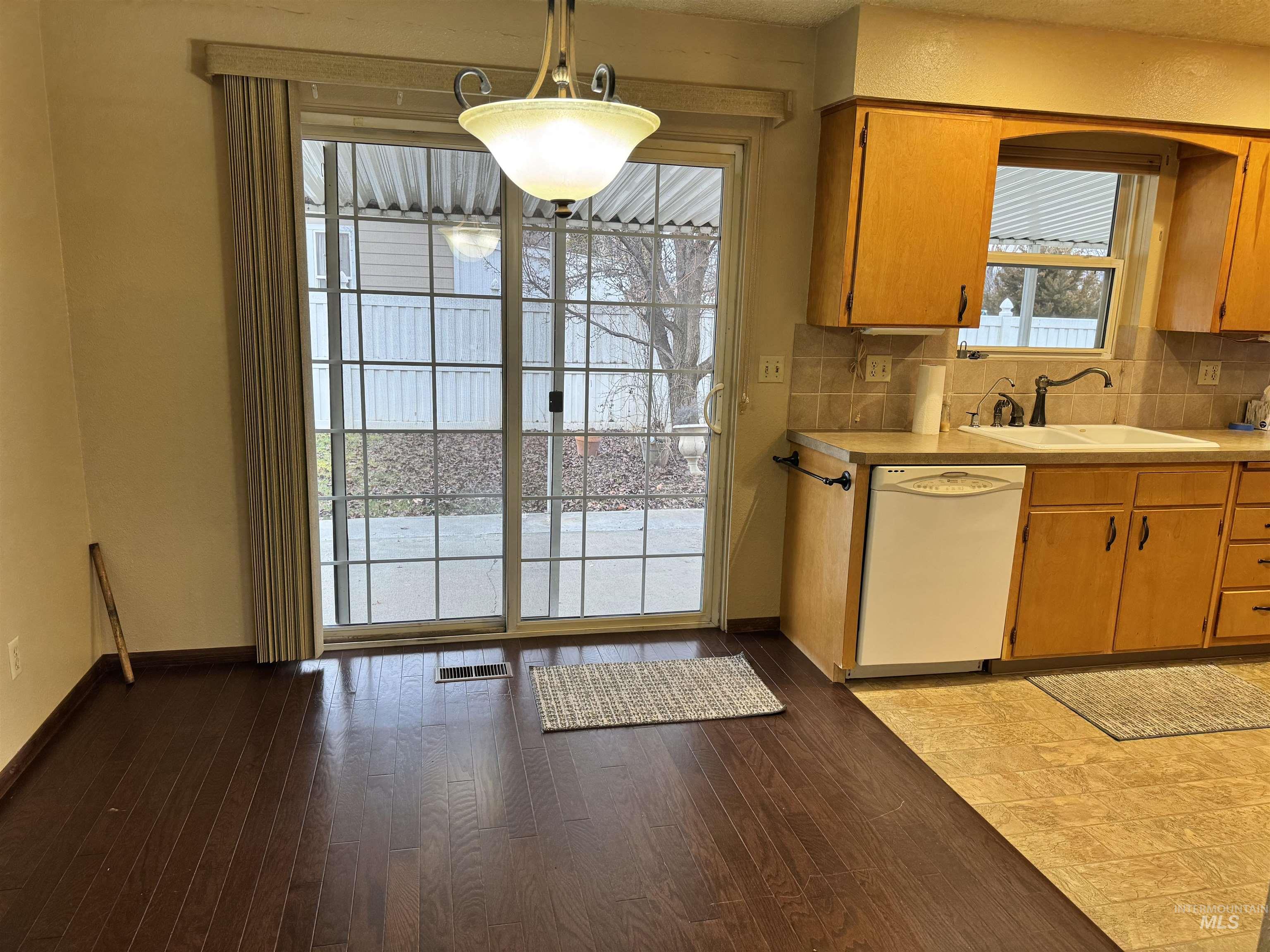 Kitchen featuring backsplash, white dishwasher, pendant lighting, light countertops, and light wood-type flooring