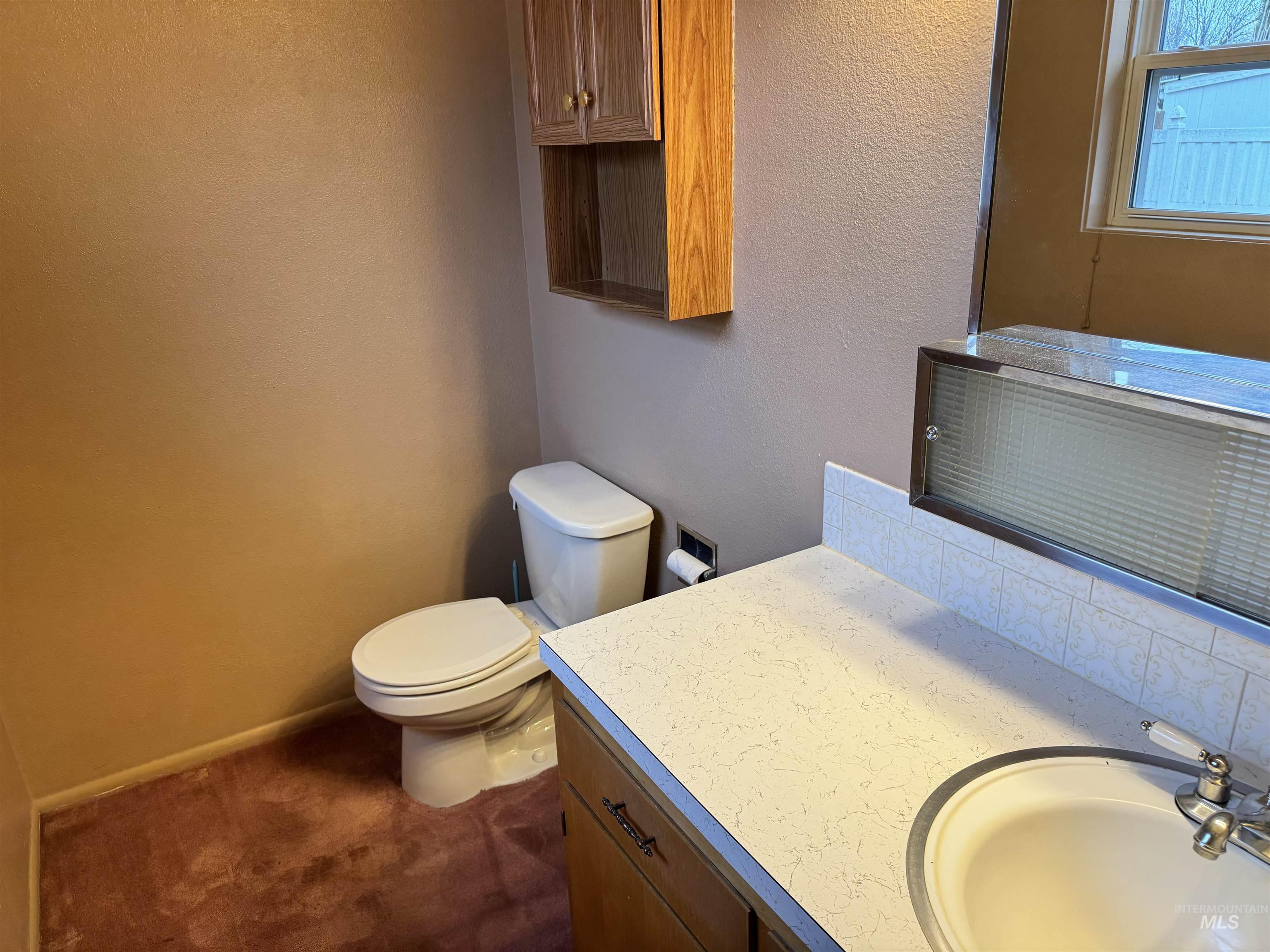 Half bath featuring a textured wall, vanity, dark colored carpet, and backsplash
