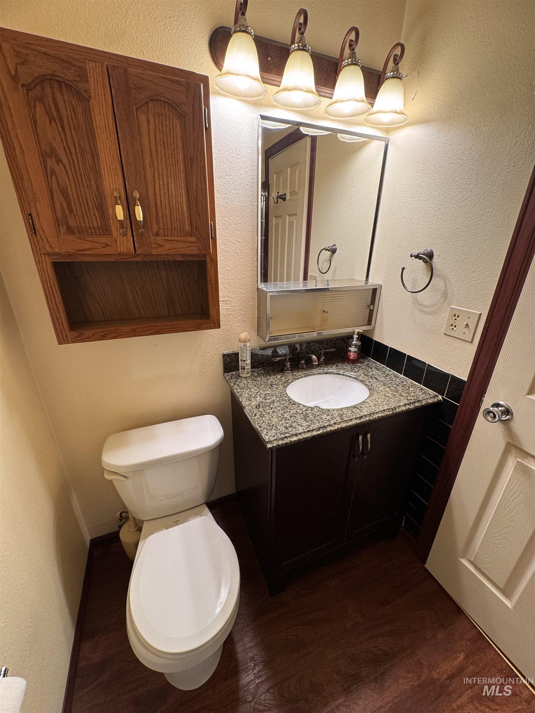 Bathroom with a textured wall, vanity, and dark wood finished floors