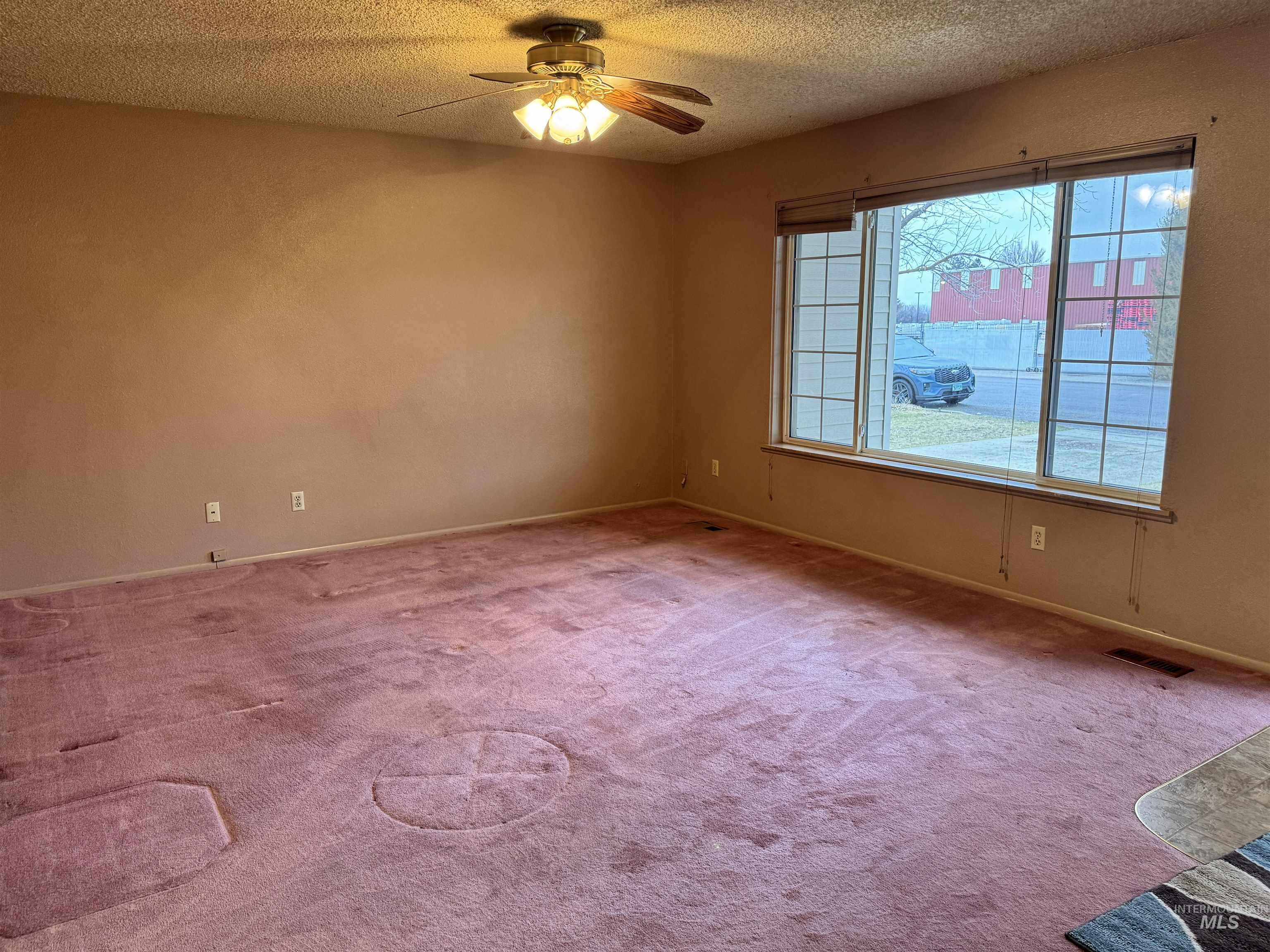 Carpeted empty room with a textured ceiling and ceiling fan
