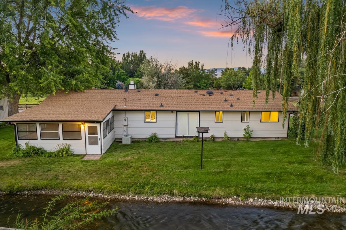 Back of house at dusk with roof with shingles, a yard, and a water view