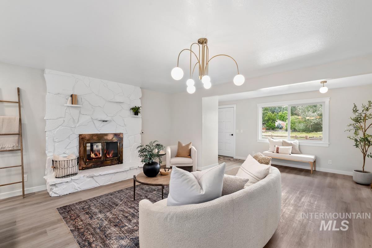 Living room with wood finished floors, a stone fireplace, and a chandelier