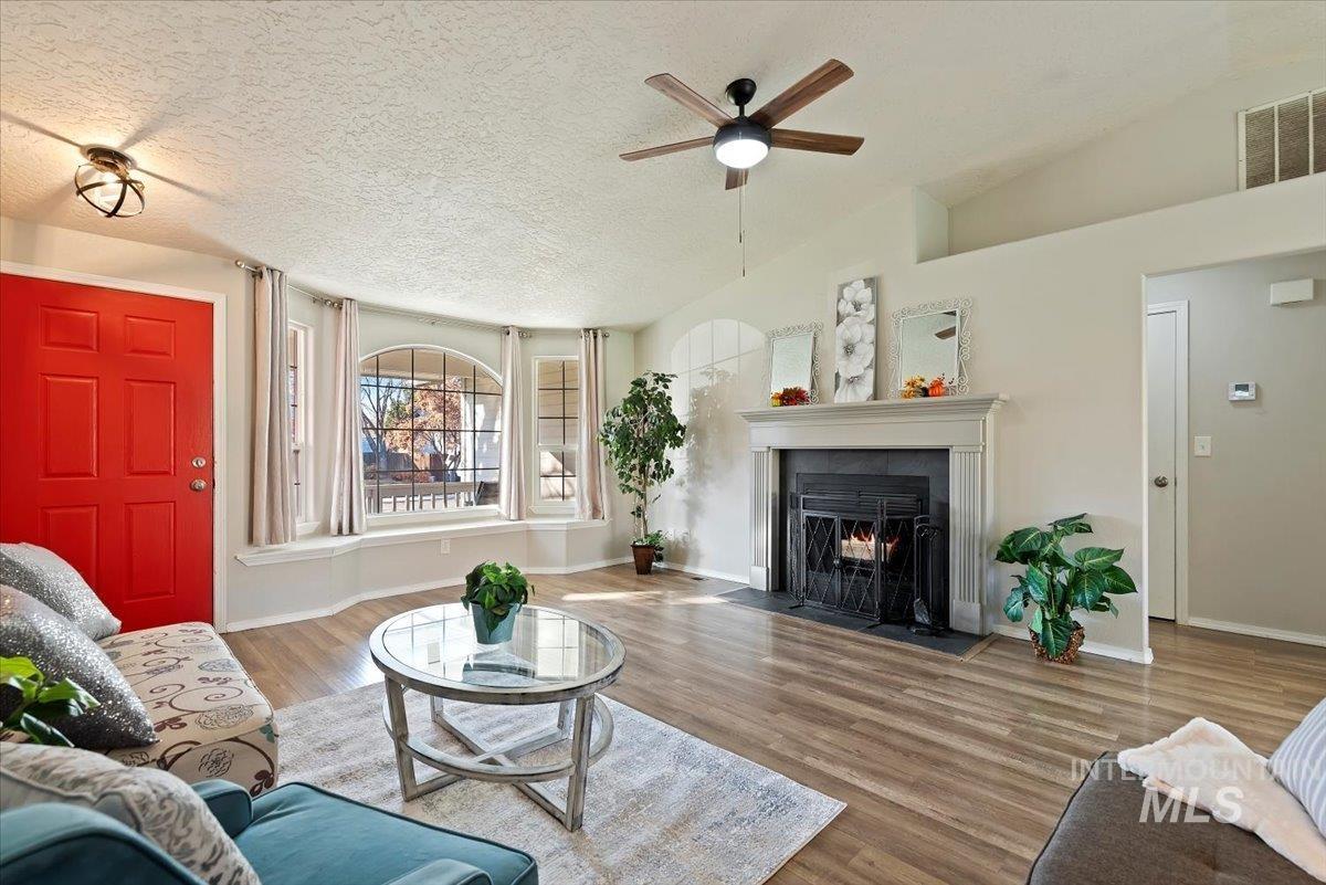 Living room featuring wood finished floors, a fireplace with flush hearth, ceiling fan, a textured ceiling, and lofted ceiling