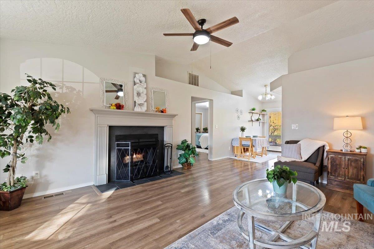 Living room featuring a textured ceiling, wood finished floors, a warm lit fireplace, ceiling fan, and a chandelier
