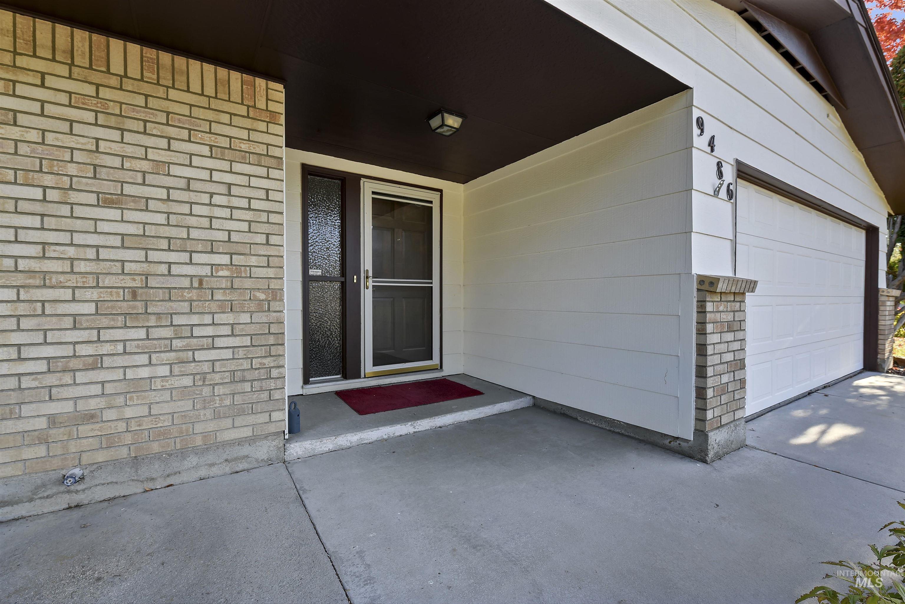 View of exterior entry with a garage, brick siding, and a patio area