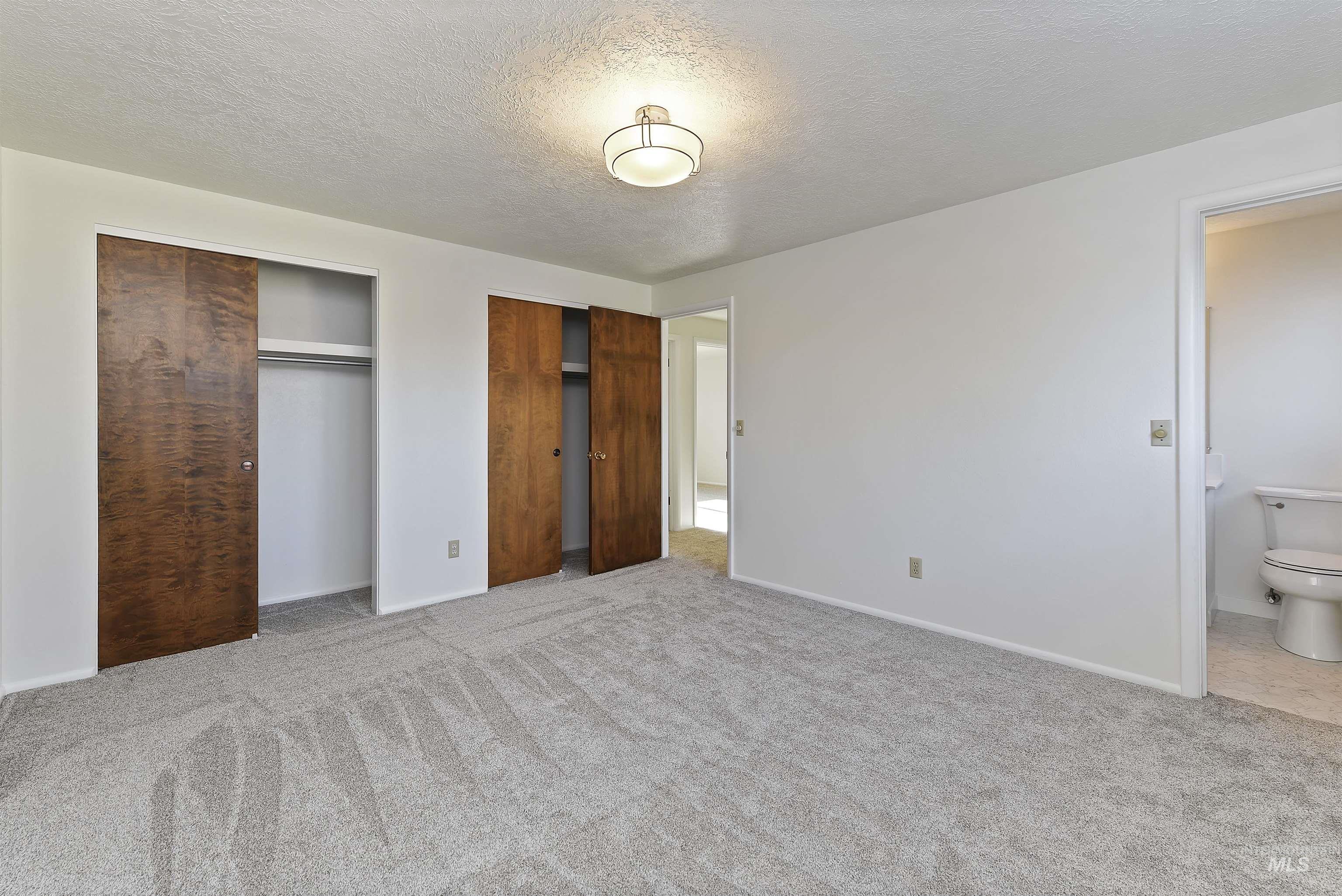 Unfurnished bedroom with two closets, a textured ceiling, and light colored carpet