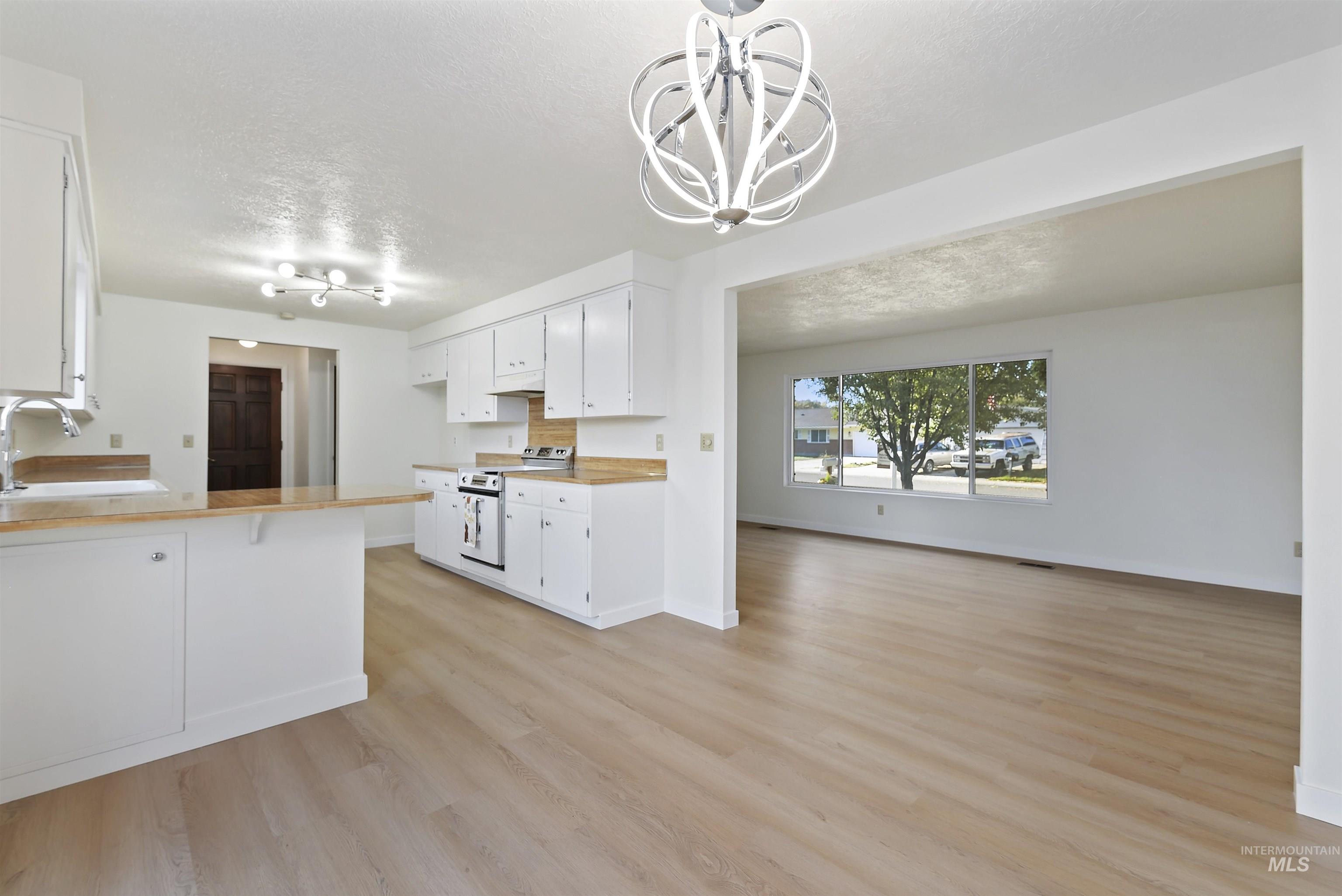 Kitchen featuring a peninsula, white cabinets, open floor plan, a textured ceiling, and range with electric cooktop