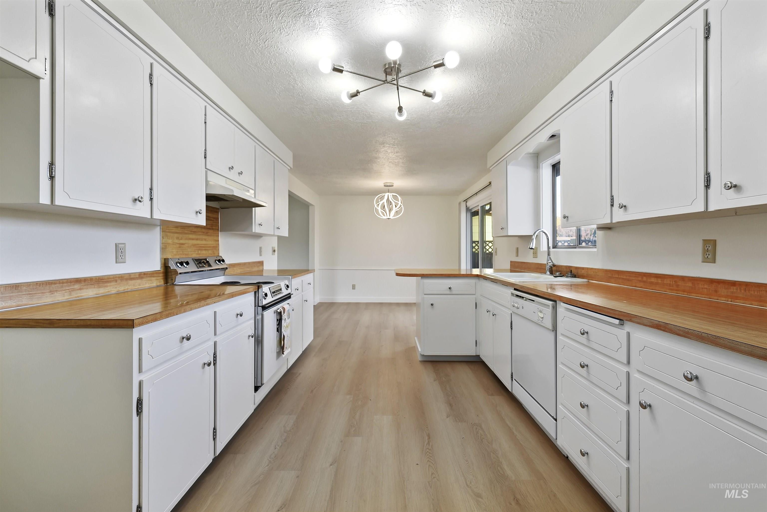 Kitchen featuring a chandelier, range with electric cooktop, light wood-style floors, a textured ceiling, and white dishwasher