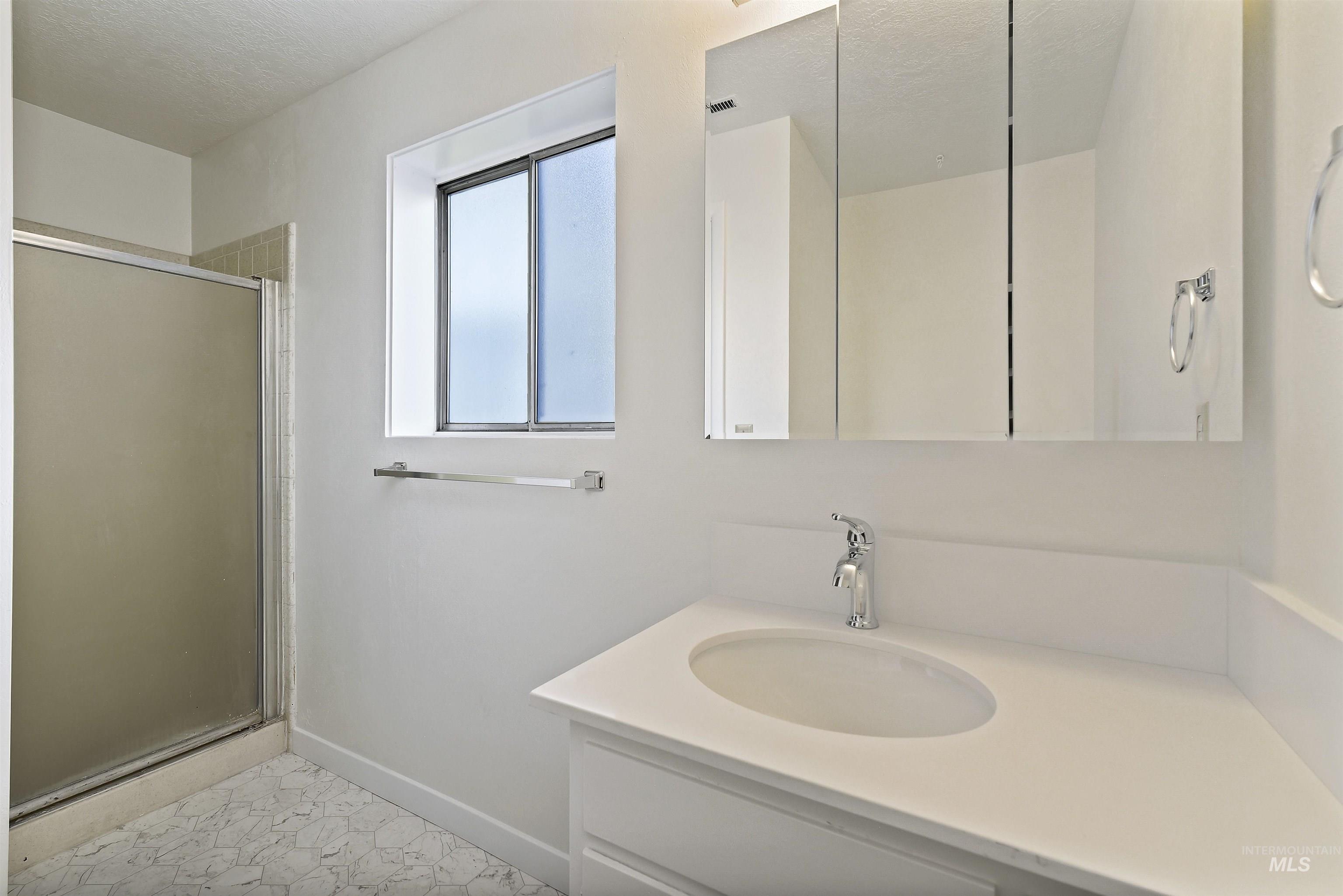 Full bathroom featuring vanity, a shower stall, a textured ceiling, and light tile patterned floors