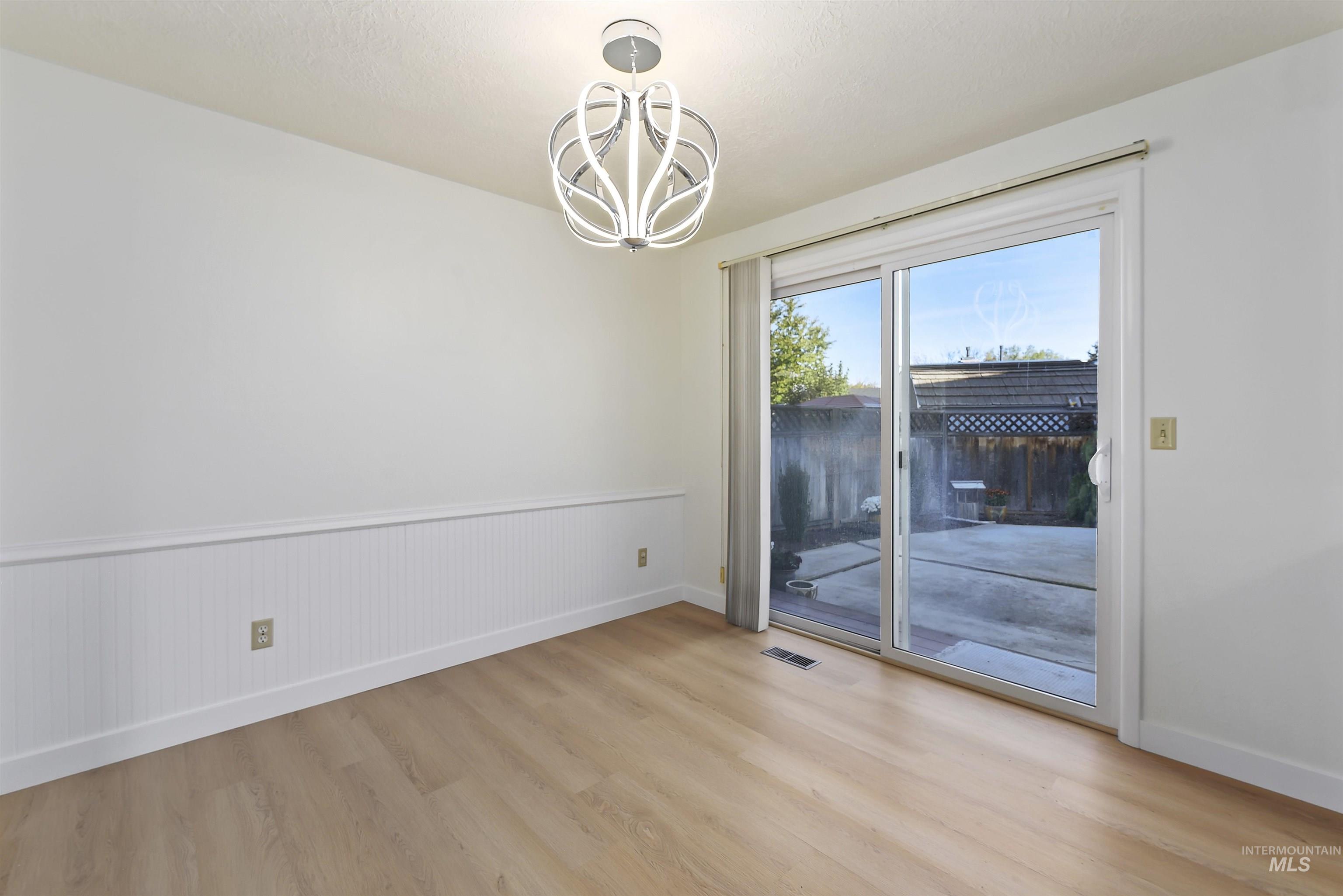 Unfurnished room with light wood finished floors, a chandelier, and a wainscoted wall