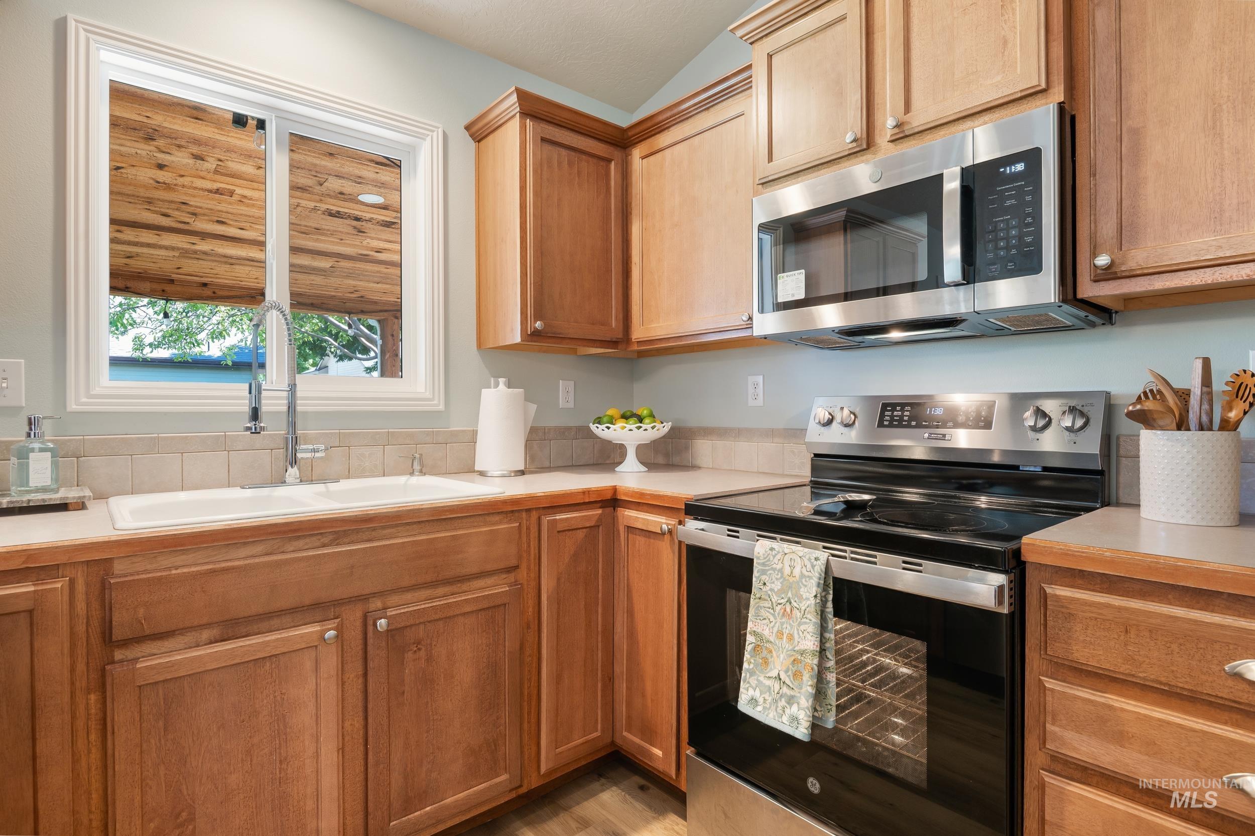 Kitchen with appliances with stainless steel finishes, light countertops, brown cabinets, and vaulted ceiling