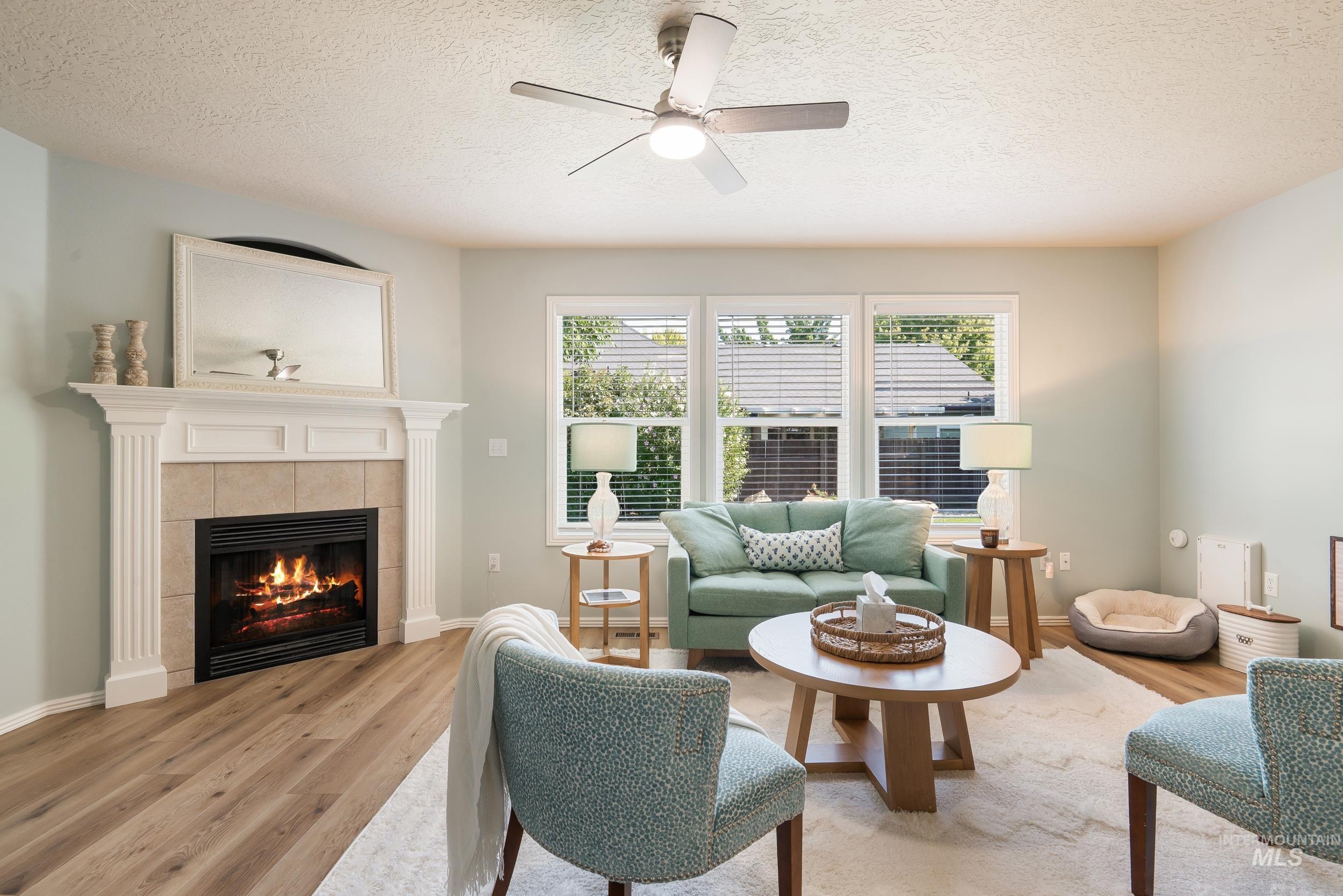 Living room with light wood-type flooring, a textured ceiling, a tiled fireplace, and ceiling fan