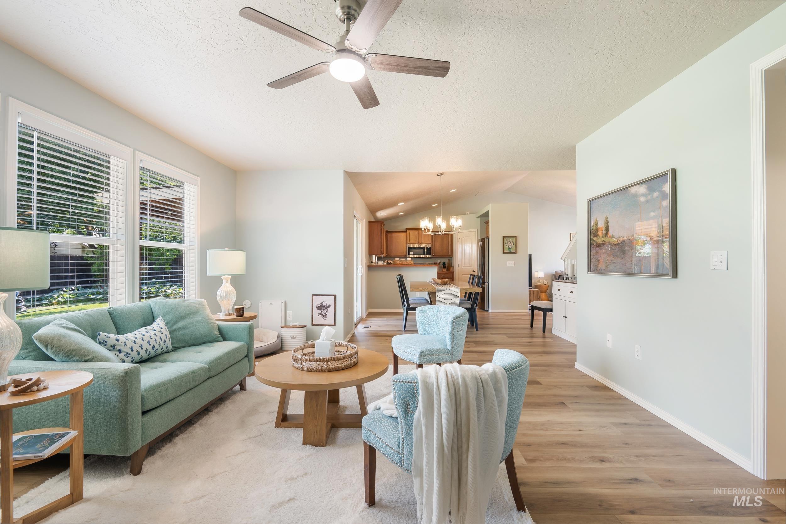 Living room with vaulted ceiling, light wood-style flooring, a chandelier, a textured ceiling, and ceiling fan