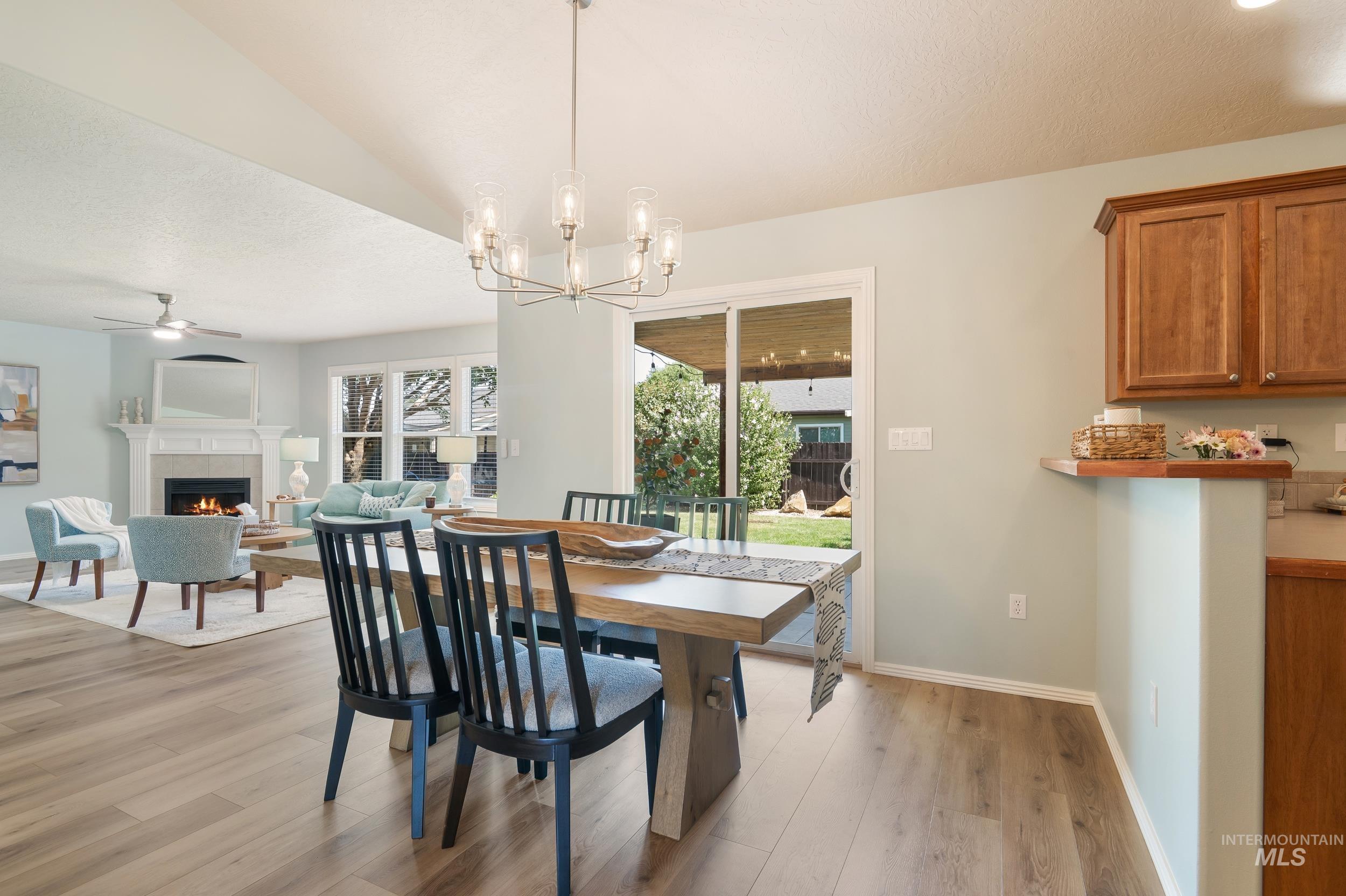 Dining area featuring a fireplace, light wood-style flooring, a textured ceiling, a chandelier, and ceiling fan