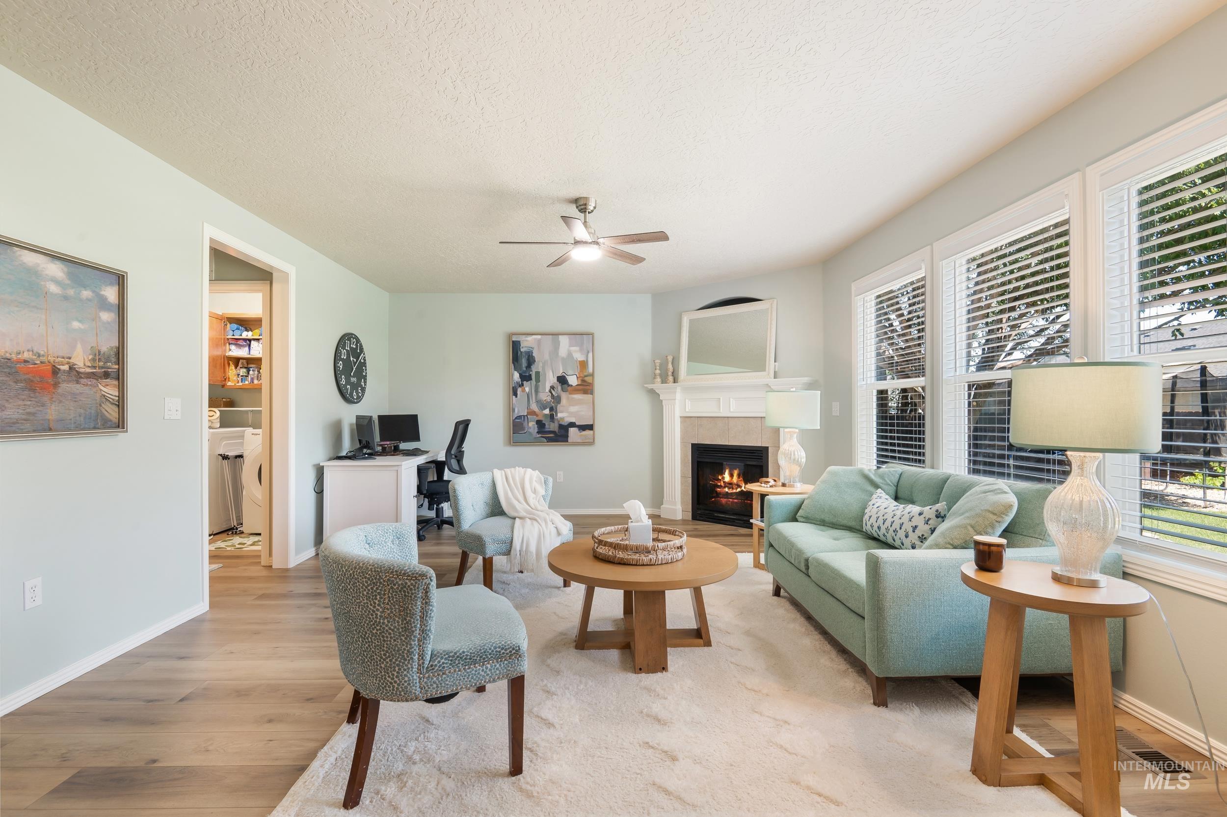 Living room with a textured ceiling, light wood-style flooring, a desk, a tile fireplace, and ceiling fan