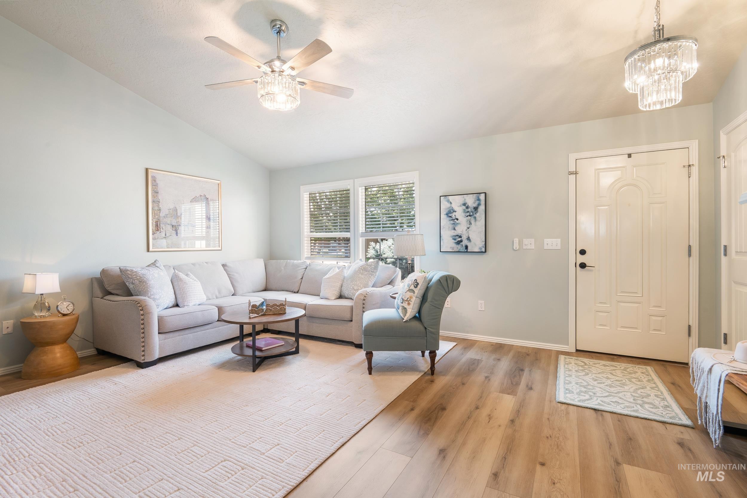 Living area featuring vaulted ceiling, light wood-type flooring, a chandelier, and a ceiling fan
