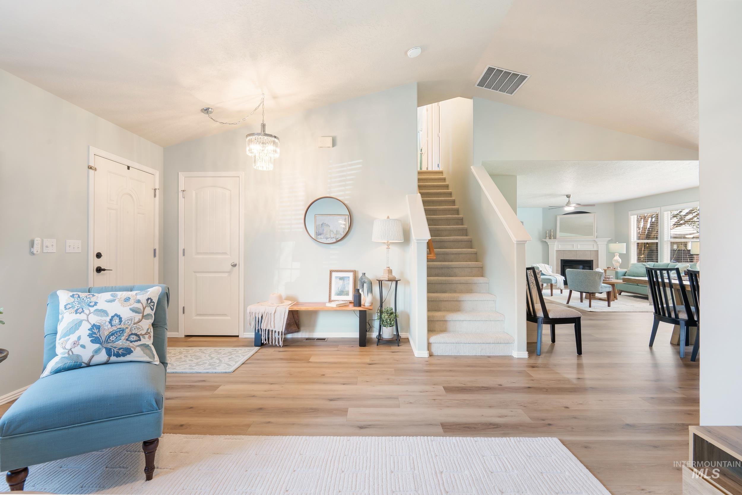 Living area featuring lofted ceiling, stairs, a fireplace, light wood-style flooring, and a chandelier