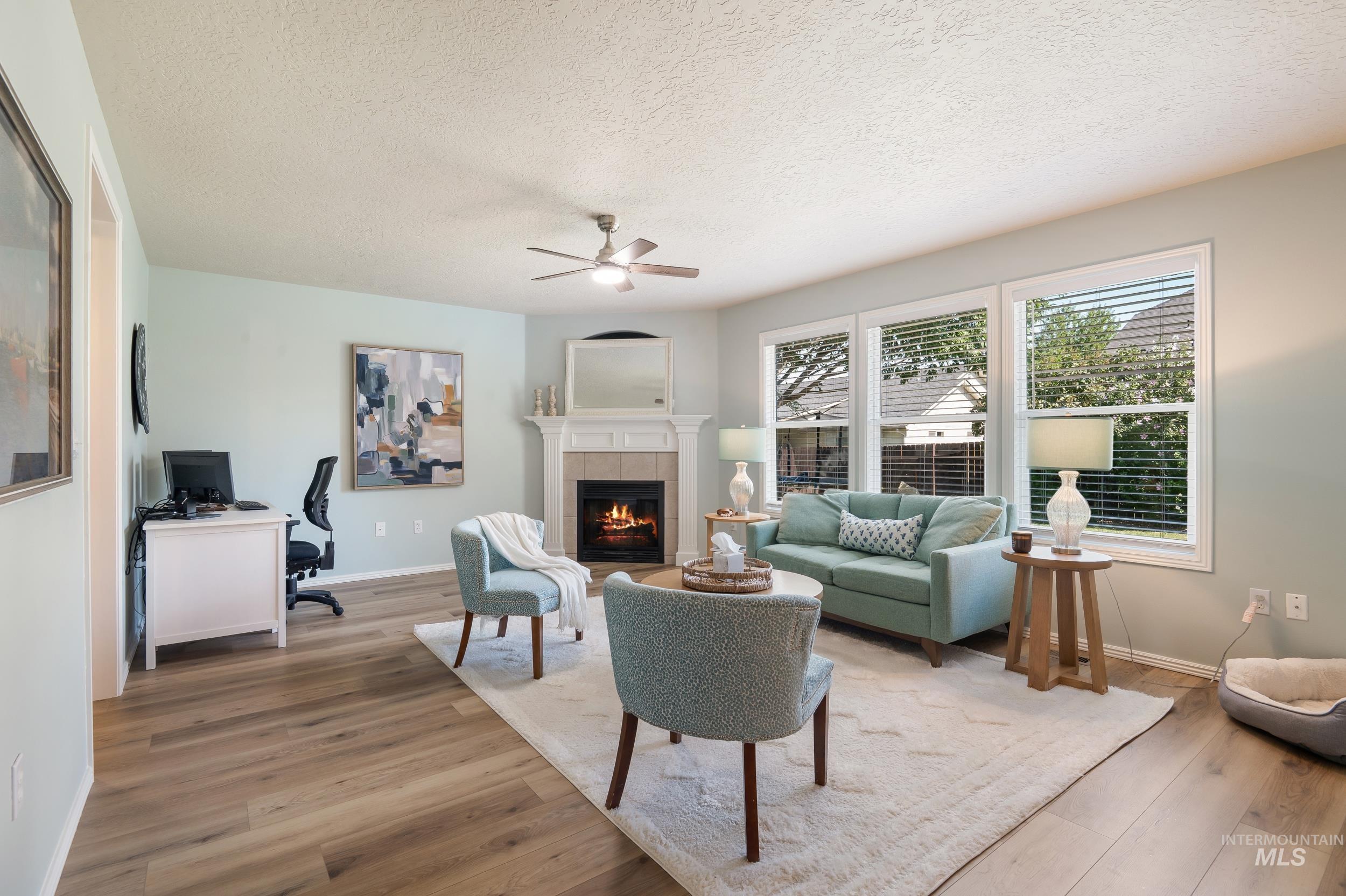 Living area featuring a textured ceiling, a desk, ceiling fan, wood finished floors, and a tiled fireplace