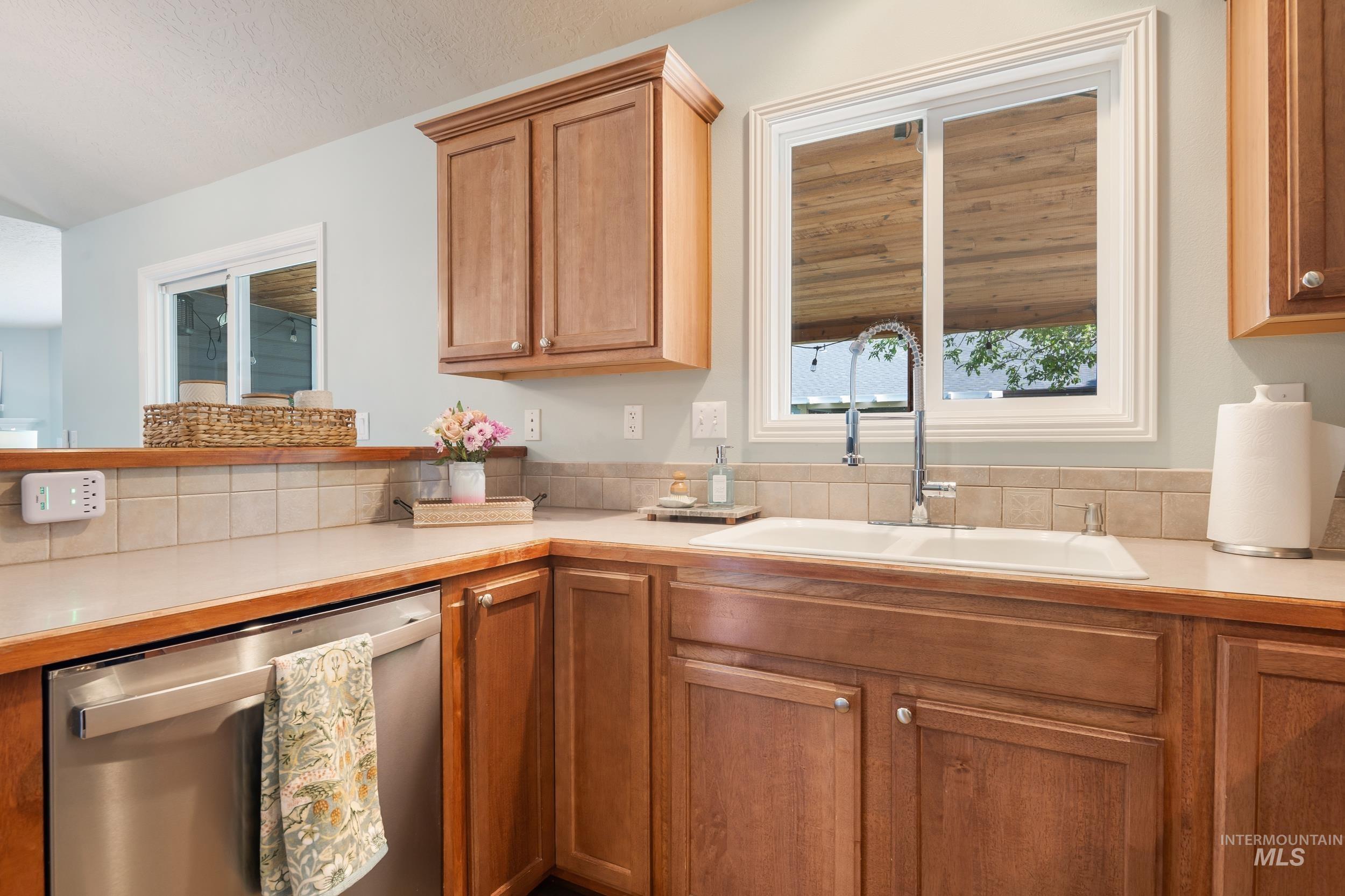 Kitchen with light countertops, stainless steel dishwasher, and brown cabinets