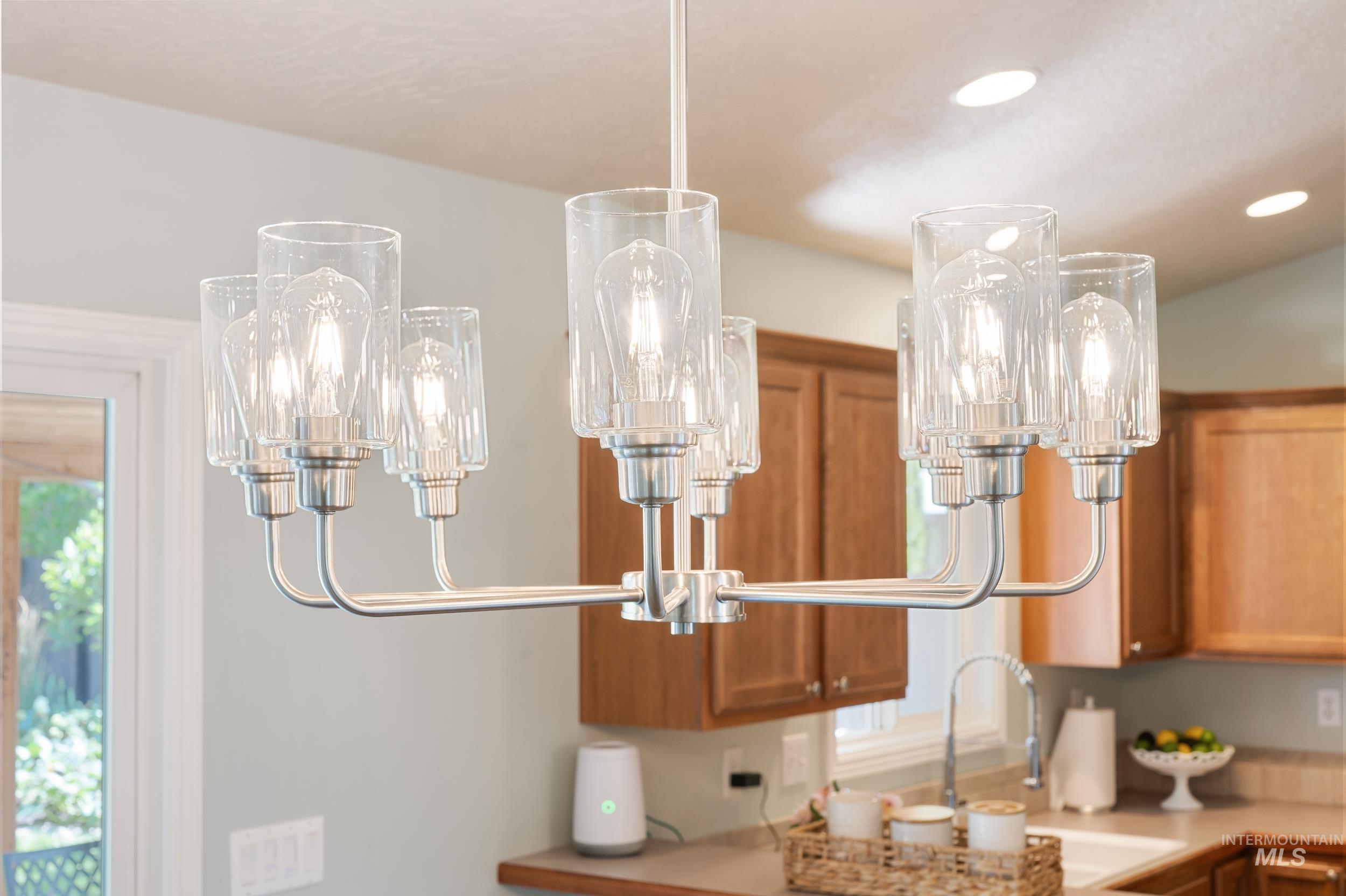 Kitchen view of brown cabinets, a chandelier, light countertops, pendant lighting, and recessed lighting