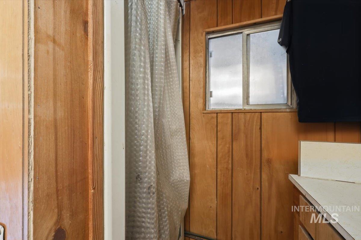 Wood-paneled interior wall featuring a sliding window with an aluminum frame, a white countertop, and a shower curtain