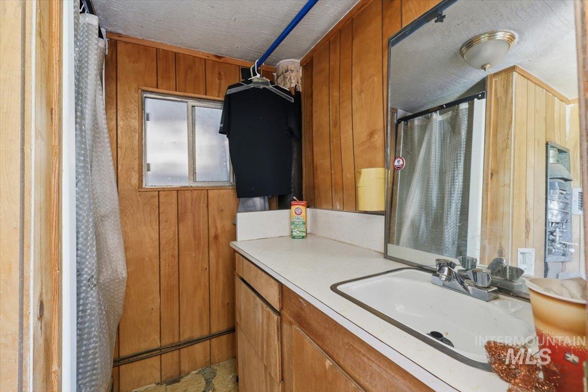 Compact bathroom featuring wood-panel walls, a white countertop with an integrated sink, and a mirrored vanity