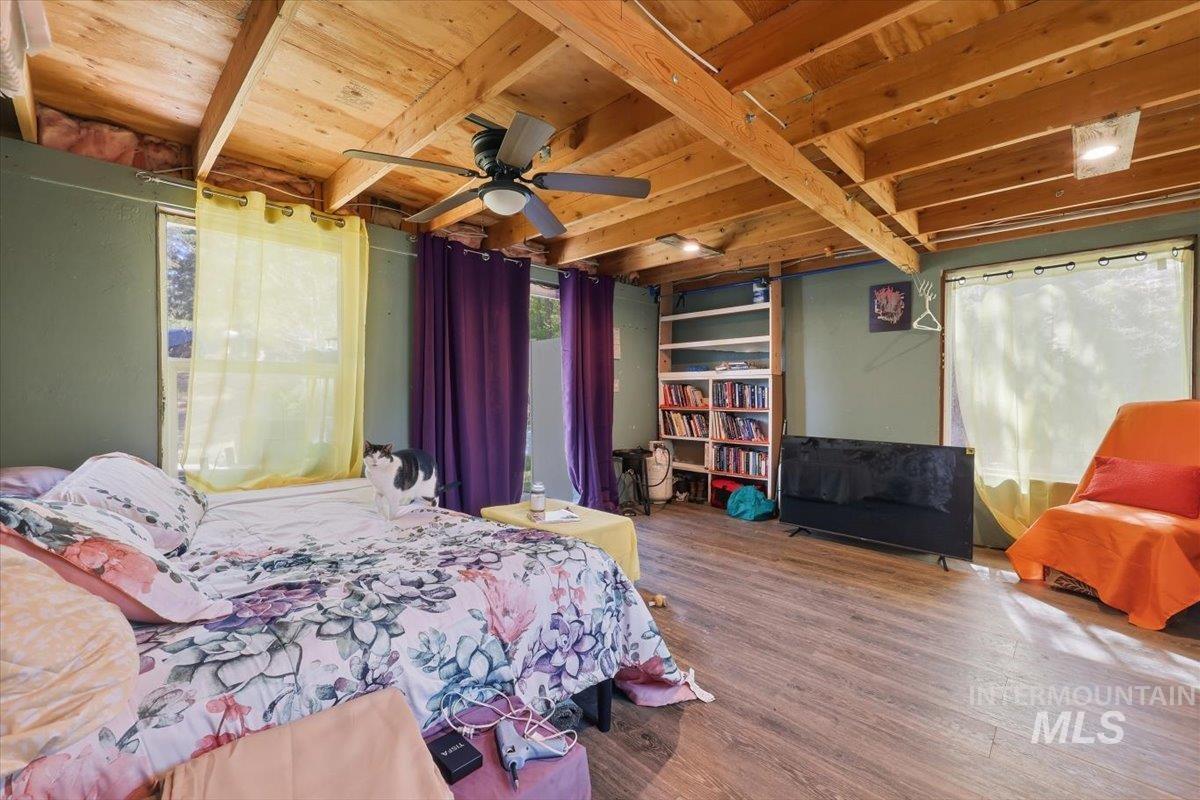 Exposed wood beam ceiling with recessed lighting and a ceiling fan, wood-finish flooring, built-in shelving, and multiple windows providing natural light