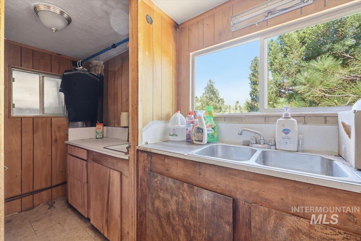 Utility area featuring wood-paneled walls and a double basin stainless steel sink with a window overlooking mature trees